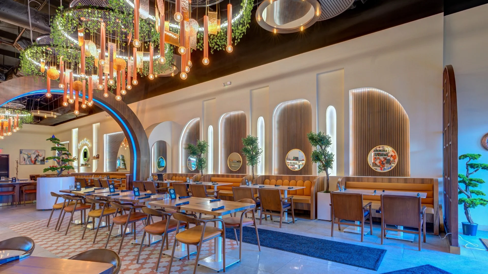 Modern restaurant interior with wooden chairs and tables, cafe-style lighting, decorative trees, and a Japanese-inspired bonsai plant, with a vibrant and inviting atmosphere.