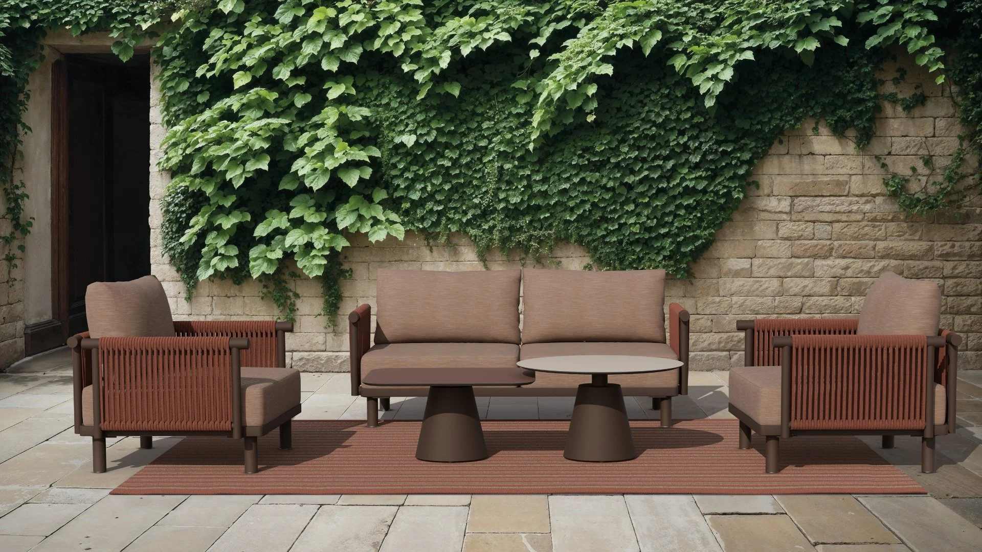 Outdoor patio area with a brown cushioned sofa, two matching armchairs, and two round tables on a striped rug, behind a wall covered with lush green vines and leaves.