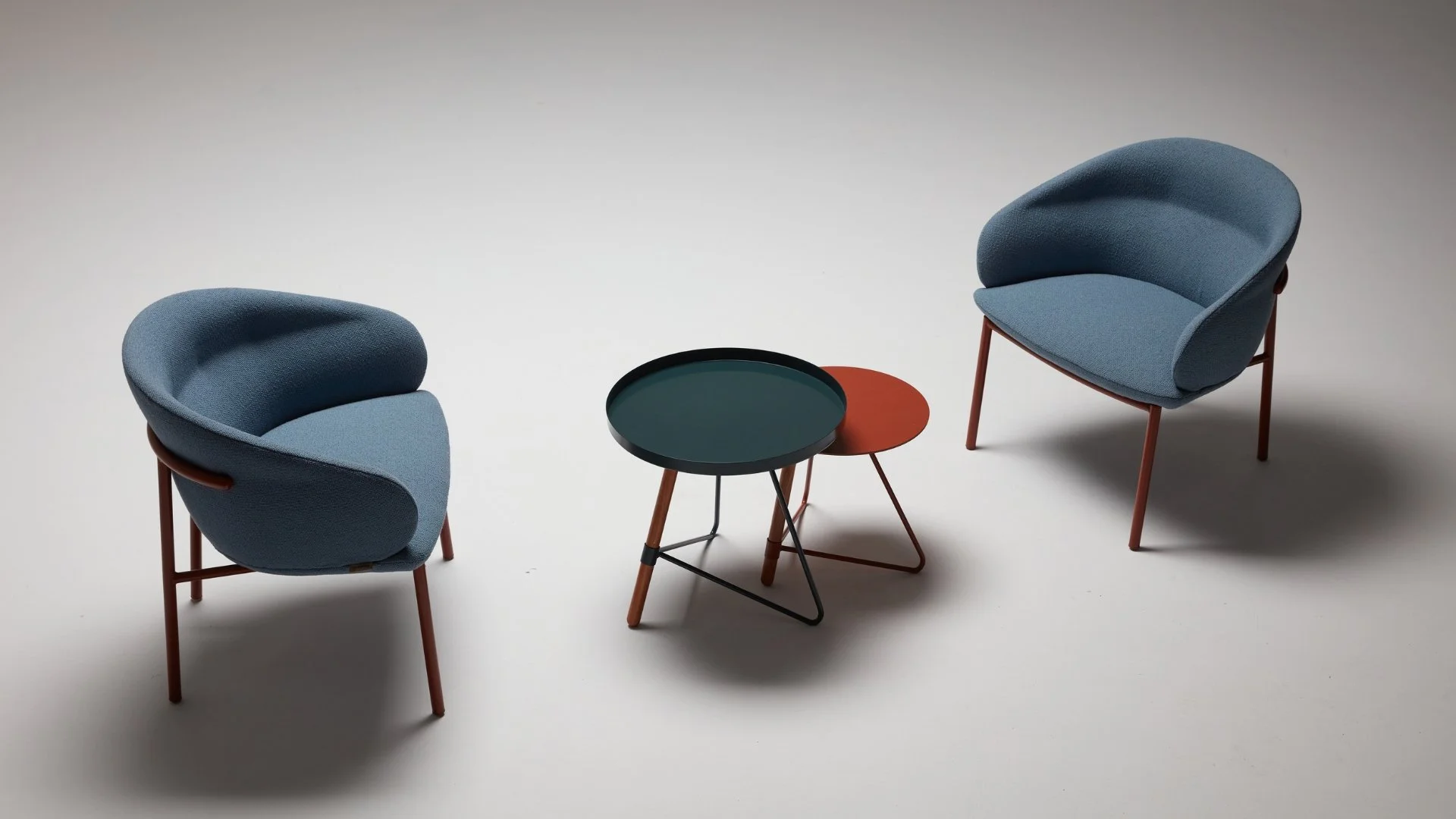 Two modern blue upholstered armchairs facing each other with two small round side tables between them, on a plain white background.