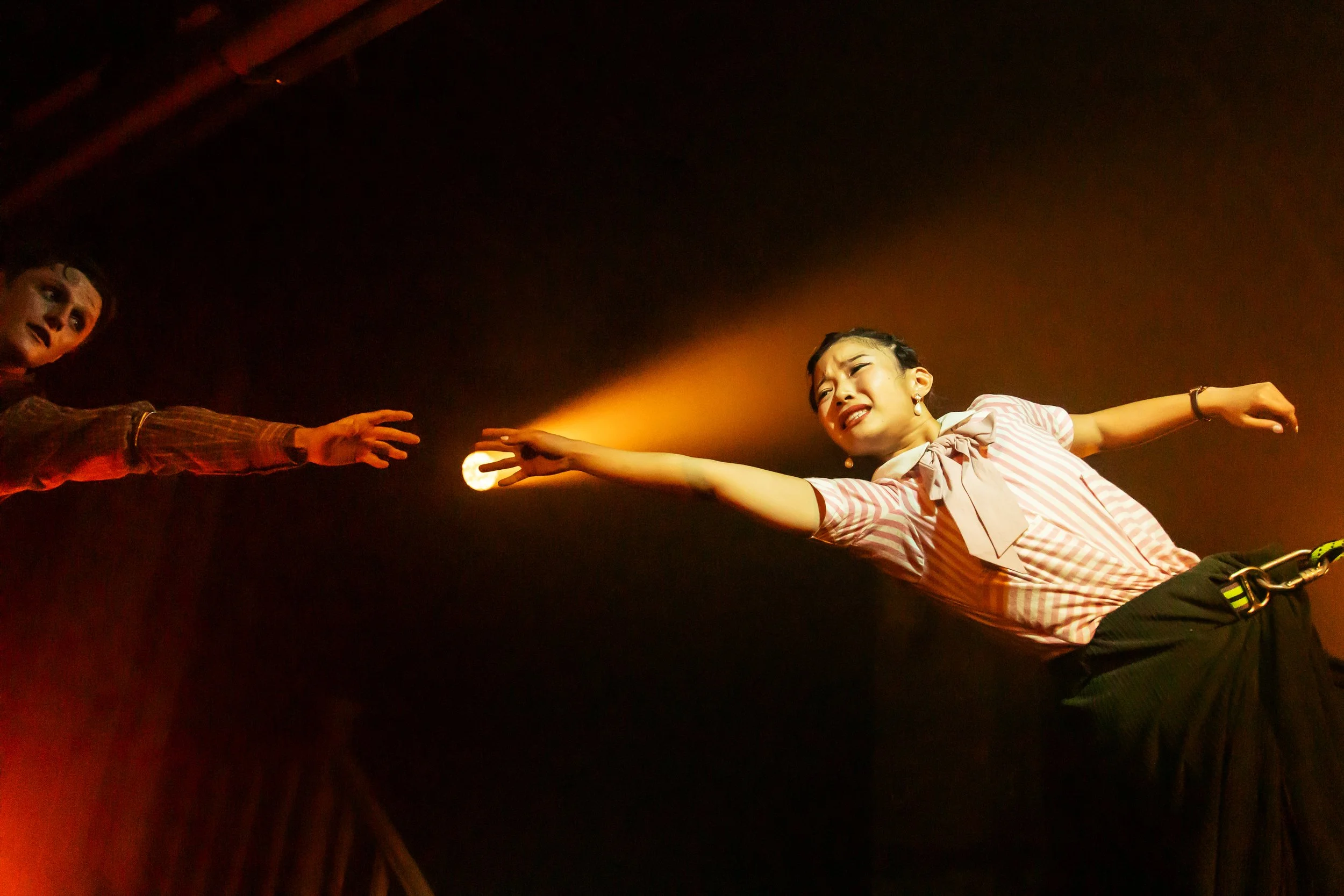 Two performers reaching out to each other on stage, one with an emotional expression, under warm stage lighting.