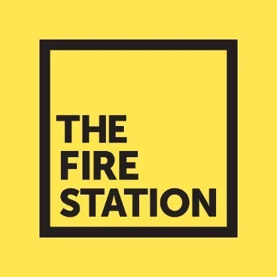 Yellow background with a black square border and the text 'THE FIRE STATION' inside in bold black letters.