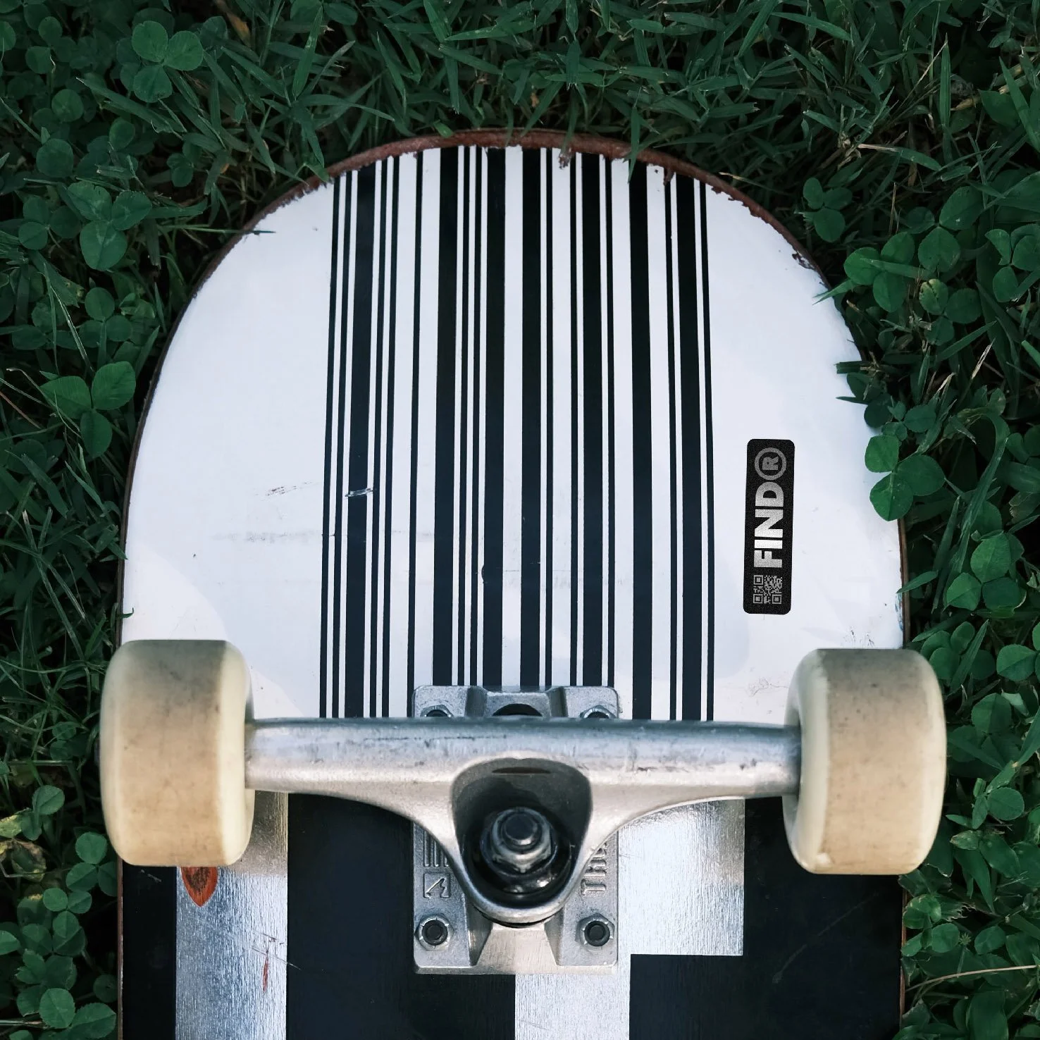 Close-up of a skateboard with a striped deck design, resting on grass.