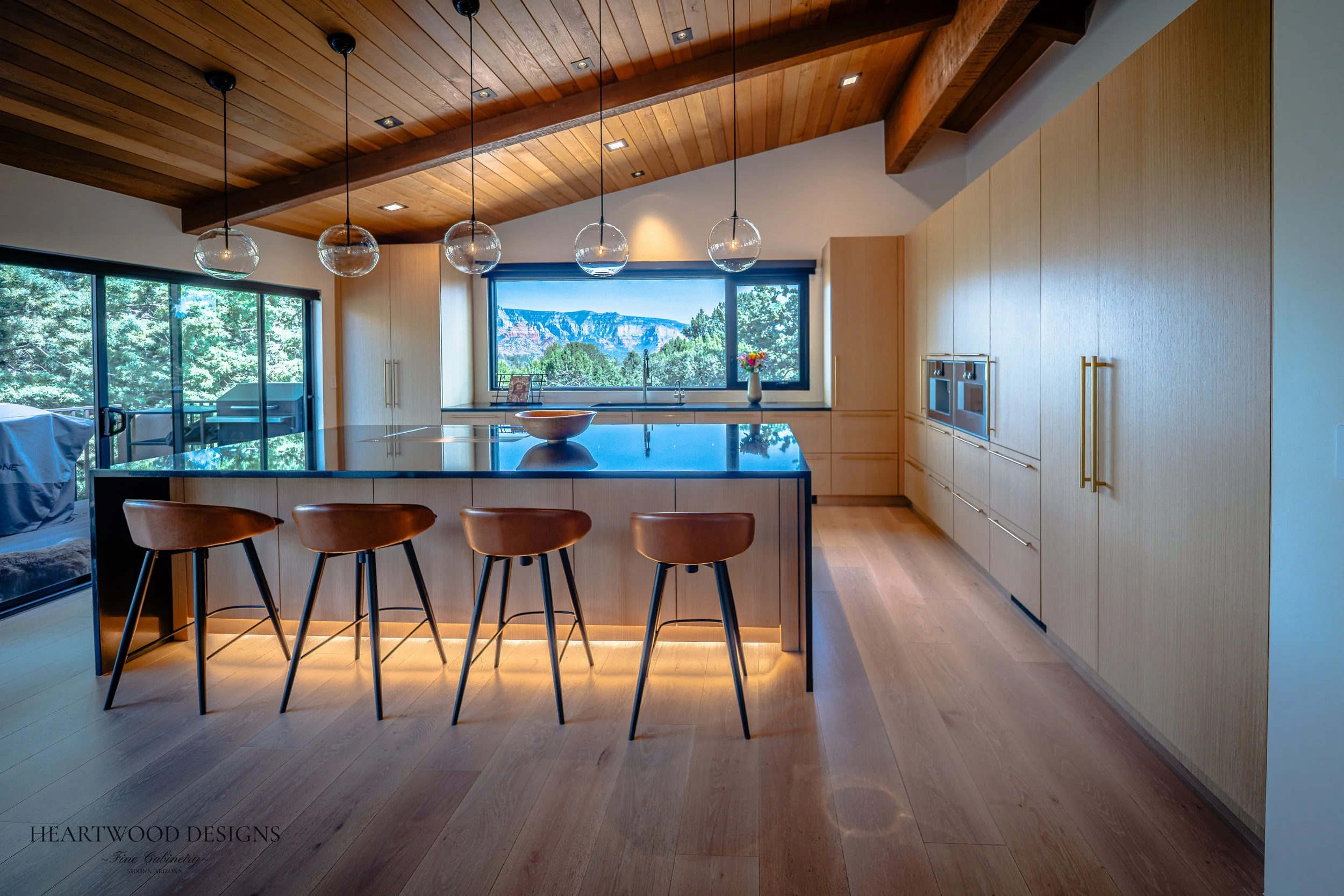 Modern kitchen remodel in Sedona featuring rift cut white oak cabinets, a large black quartz island with leather barstools, Gaggenau appliances and views of the red rocks.
