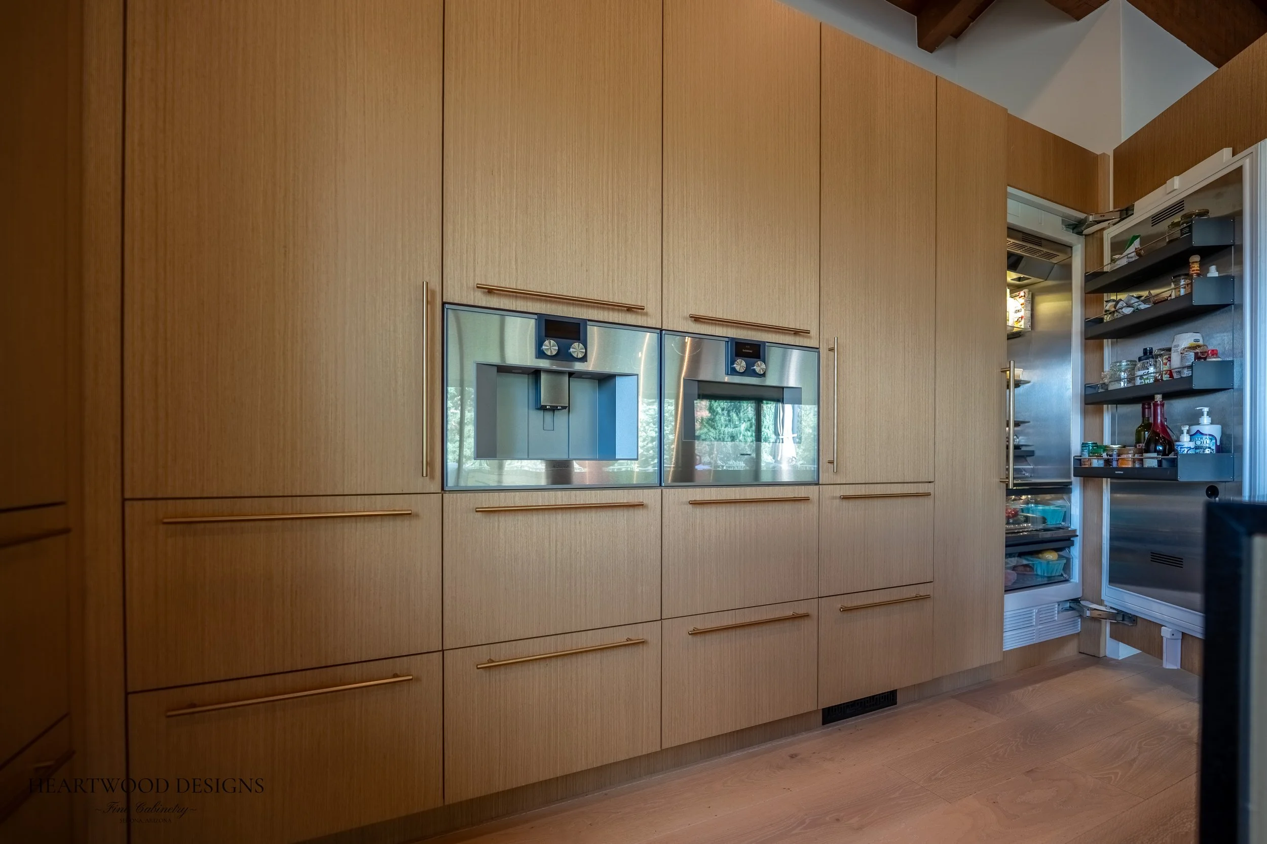 Modern kitchen remodel in Sedona featuring rift cut white oak cabinets, a large black quartz island with leather barstools, Gaggenau appliances and views of the red rocks.