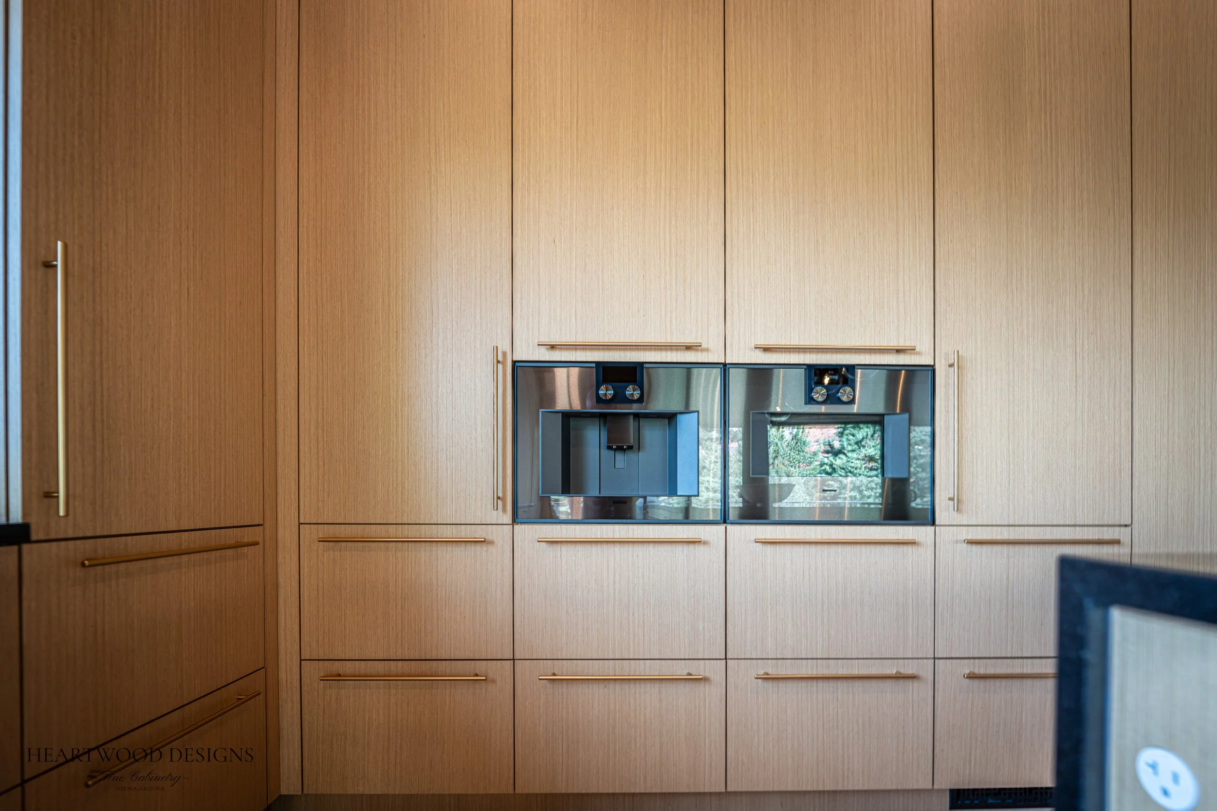 Modern kitchen remodel in Sedona featuring rift cut white oak cabinets, a large black quartz island with leather barstools, Gaggenau appliances and views of the red rocks.