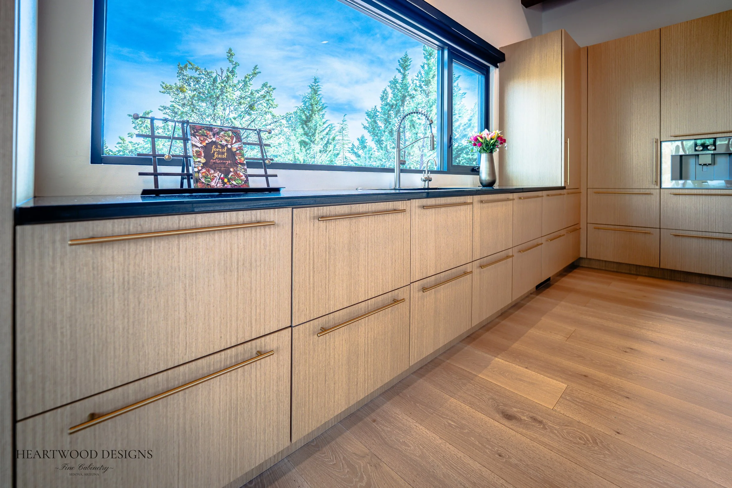 Modern kitchen remodel in Sedona featuring rift cut white oak cabinets, a large black quartz island with leather barstools, Gaggenau appliances and views of the red rocks.