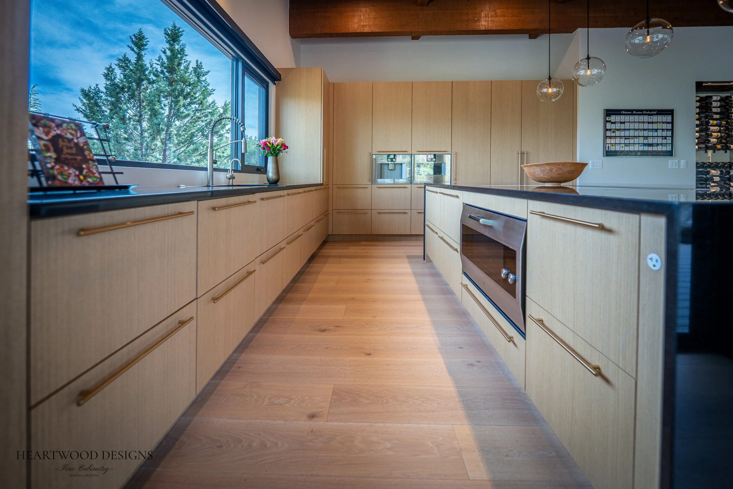 Modern kitchen remodel in Sedona featuring rift cut white oak cabinets, a large black quartz island with leather barstools, and views of the red rocks.