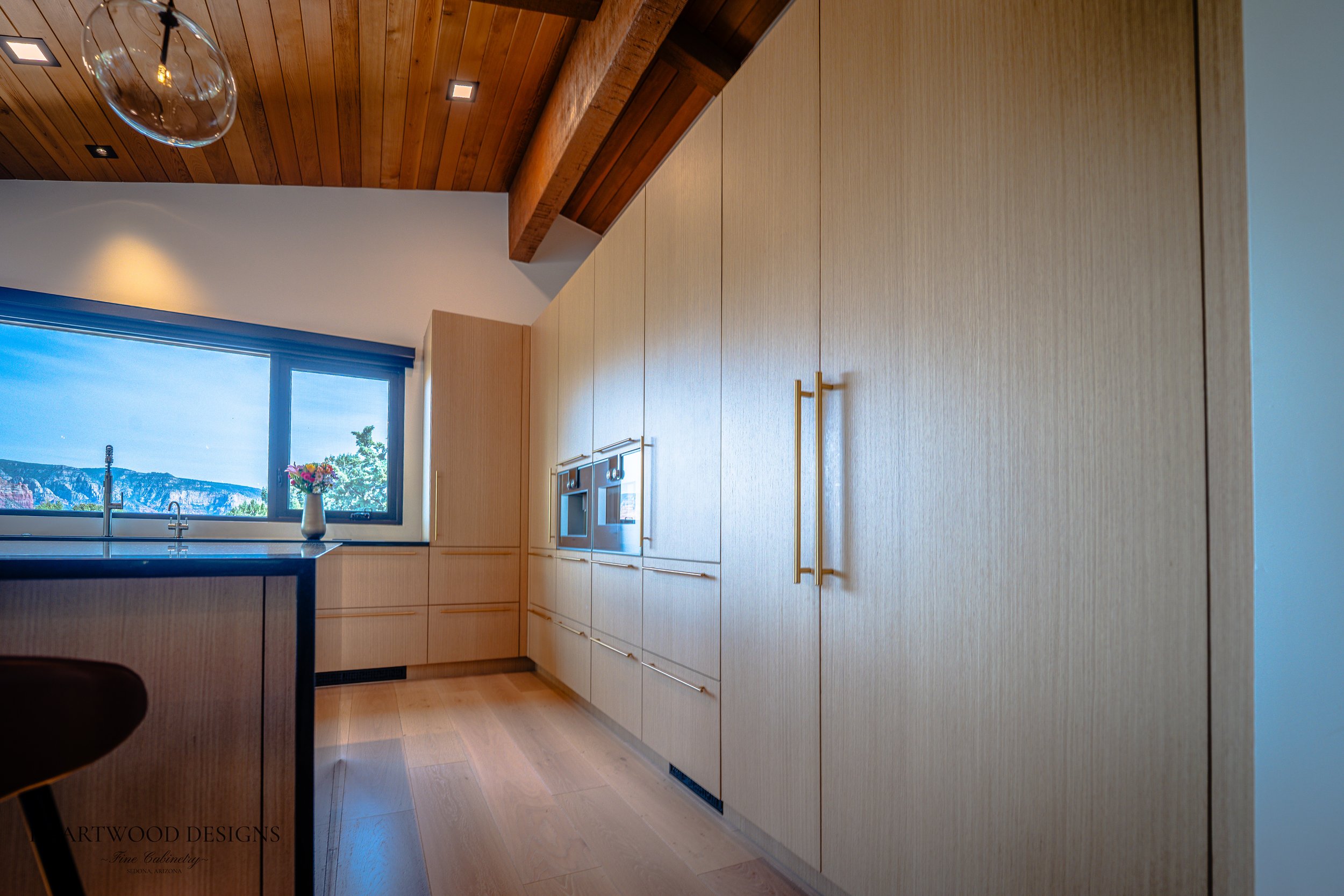 Modern kitchen remodel in Sedona featuring rift cut white oak cabinets, a large black quartz island with leather barstools, Gaggenau appliances and views of the red rocks.
