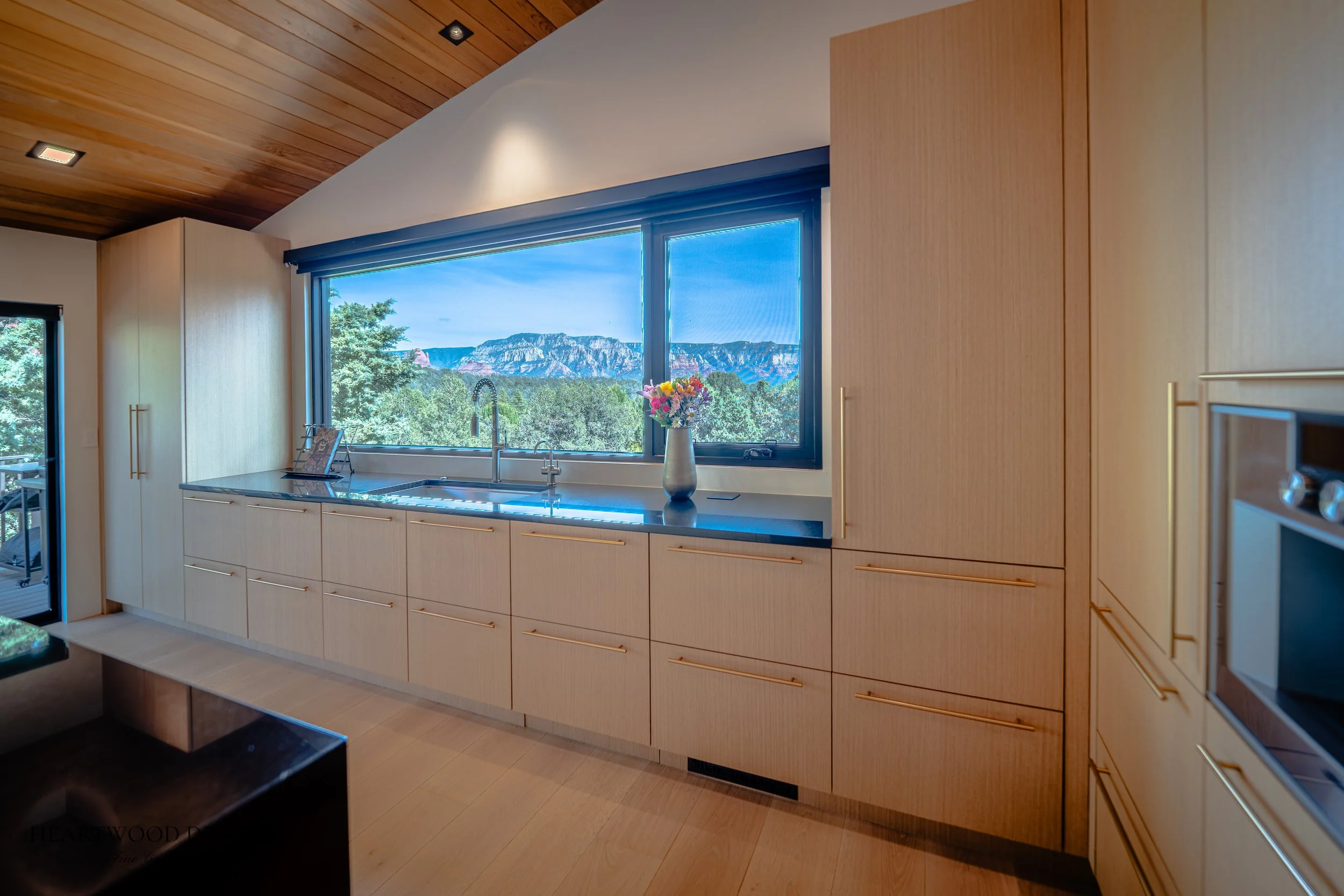 Modern kitchen remodel in Sedona featuring rift cut white oak cabinets, a large black quartz island with leather barstools, Gaggenau appliances and views of the red rocks.