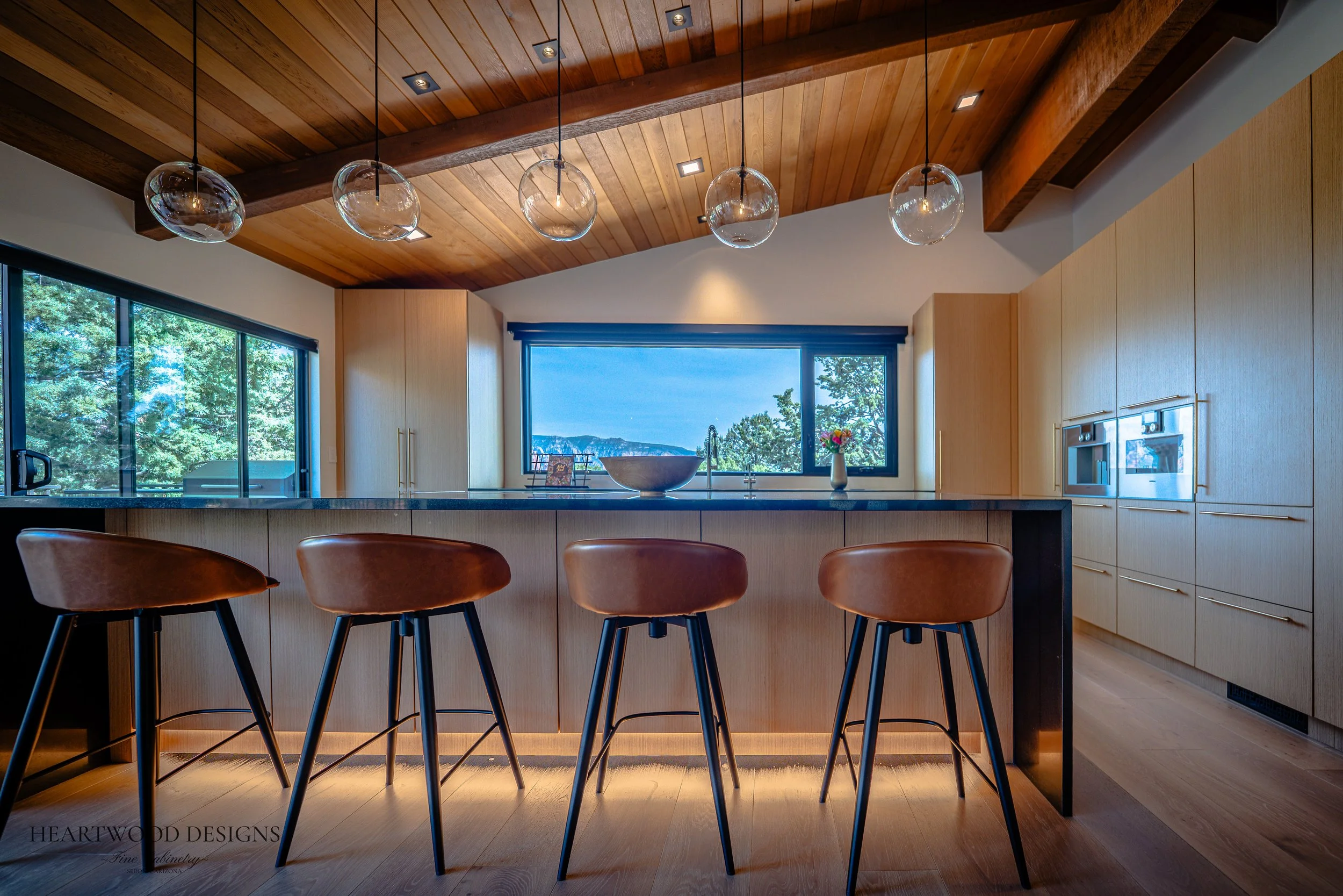Modern kitchen remodel in Sedona featuring rift cut white oak cabinets, a large black quartz island with leather barstools, Gaggenau appliances and views of the red rocks.