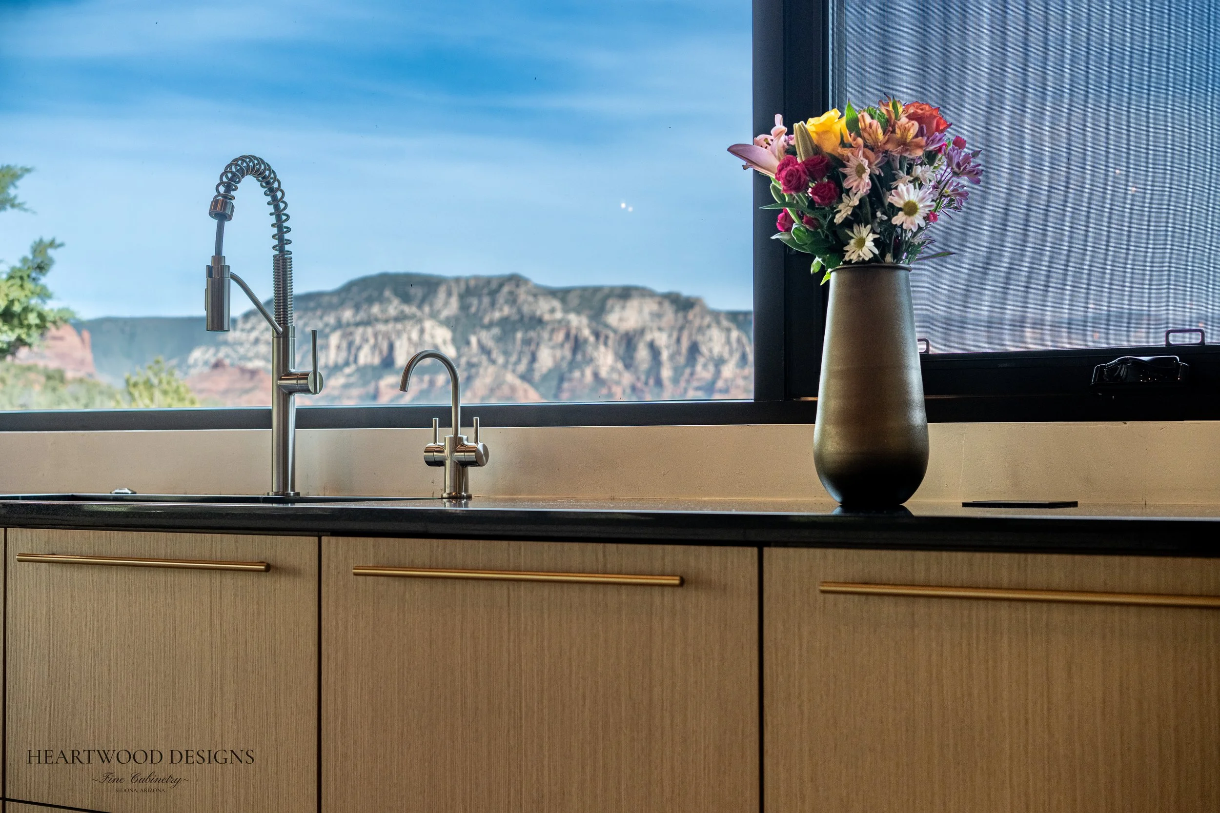 Modern kitchen remodel in Sedona featuring rift cut white oak cabinets, a large black quartz island with leather barstools, Gaggenau appliances and views of the red rocks.