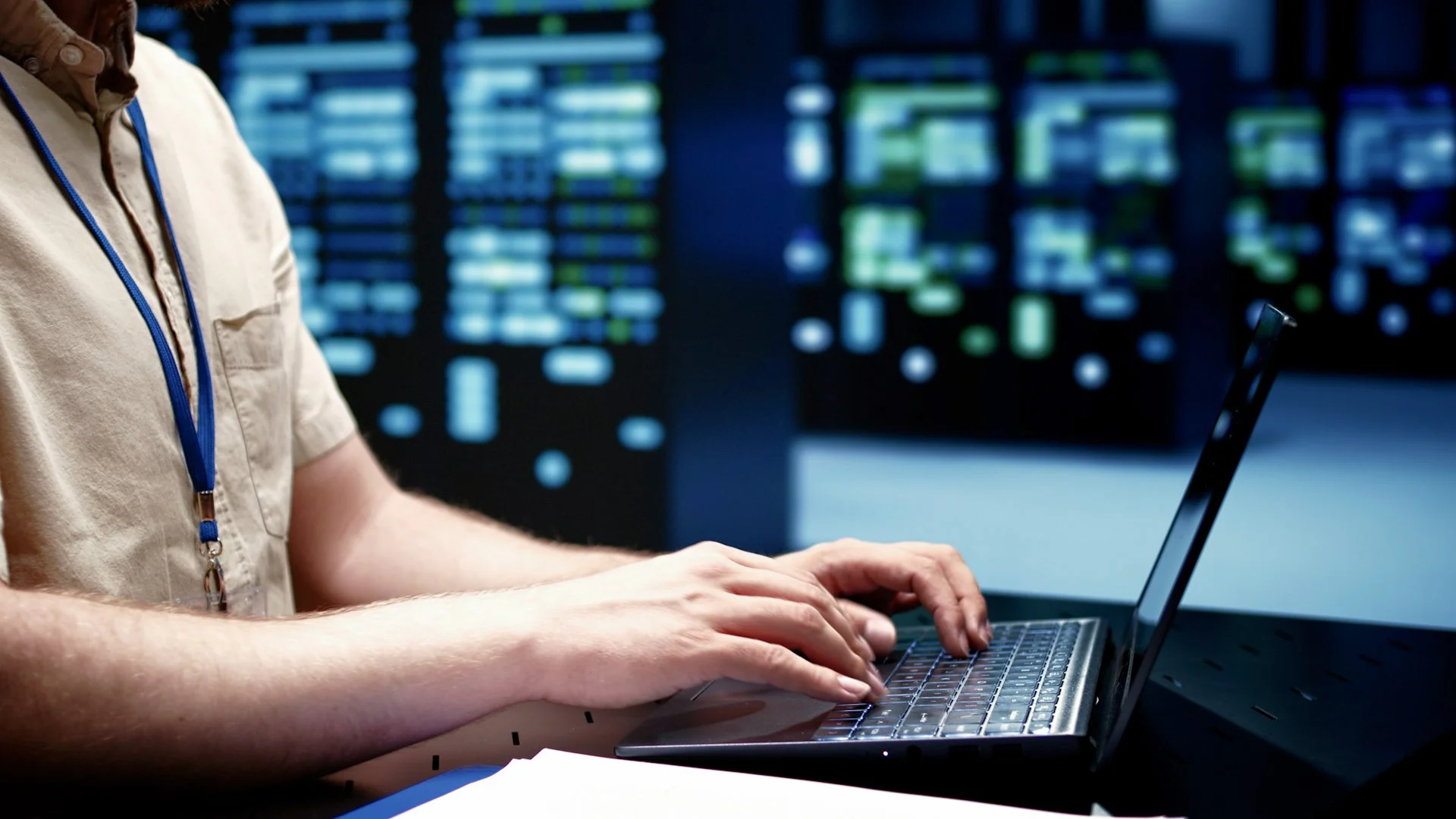IT technician with an ID badge working on a laptop in a server room.