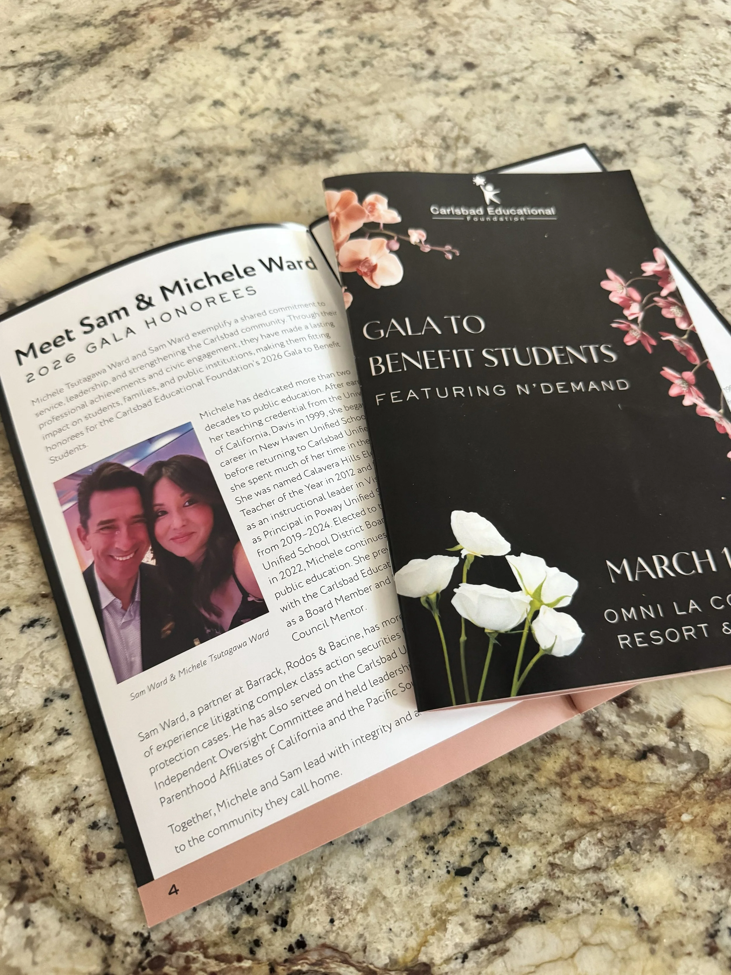 Brochure for a Gala to benefit students, featuring a floral design with pink and white flowers, and the logo of Carlsbad Educational Foundation, placed on a granite countertop.
