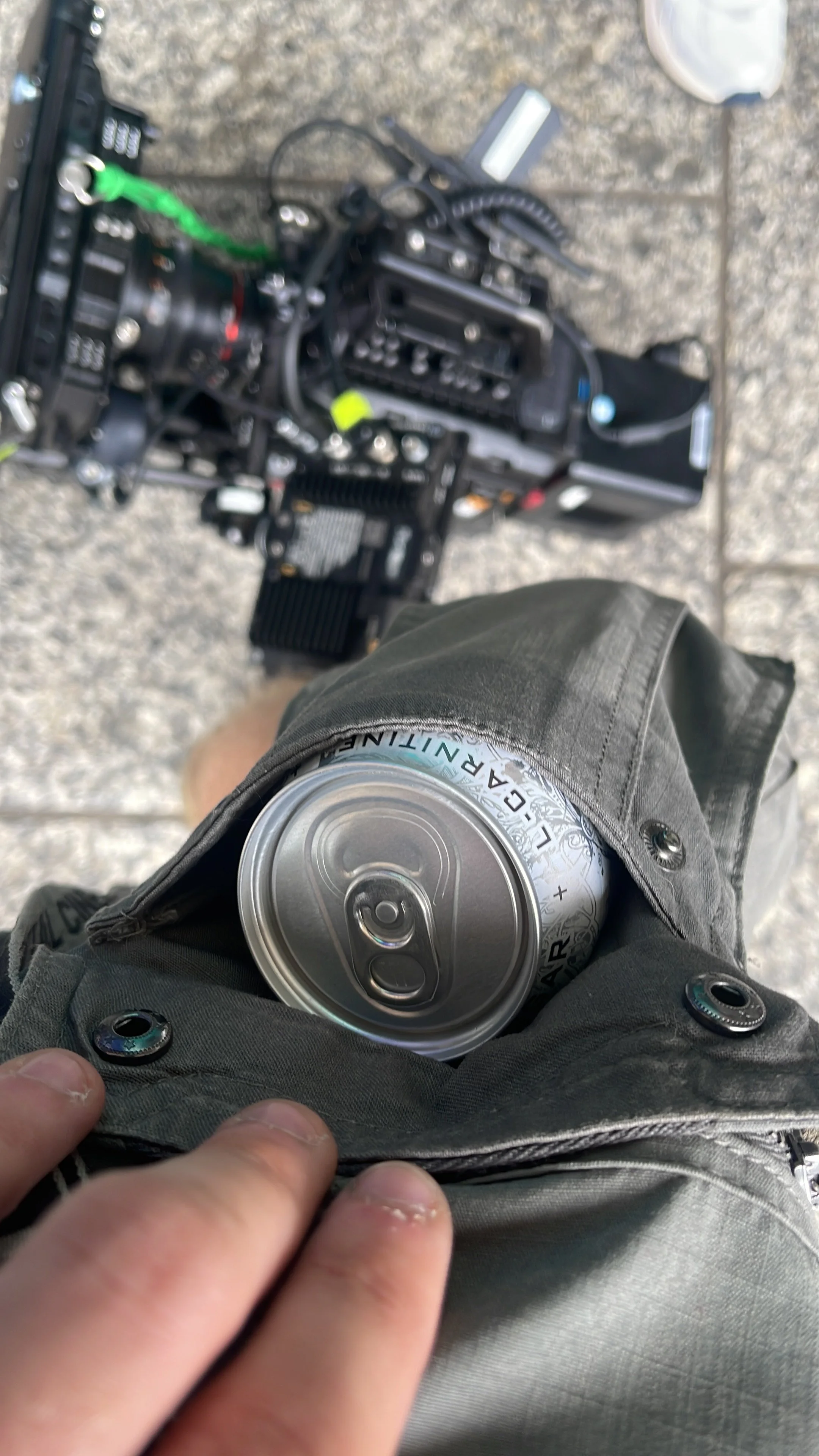 Person holding a can of LaCroix sparkling water in their lap, with a blurred view of camera equipment on the ground in the background.