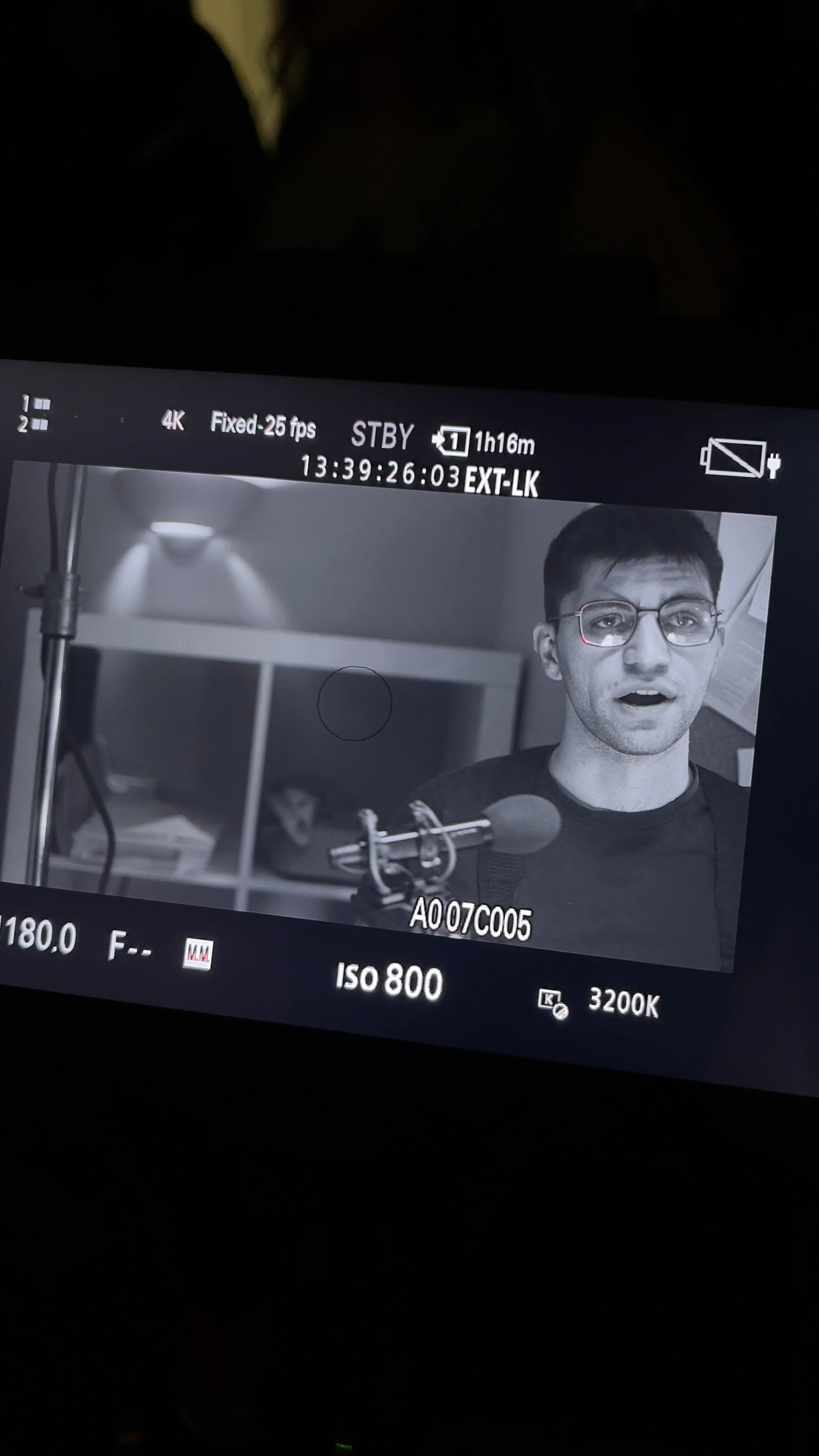 A person with glasses speaking into a microphone in a recording studio.