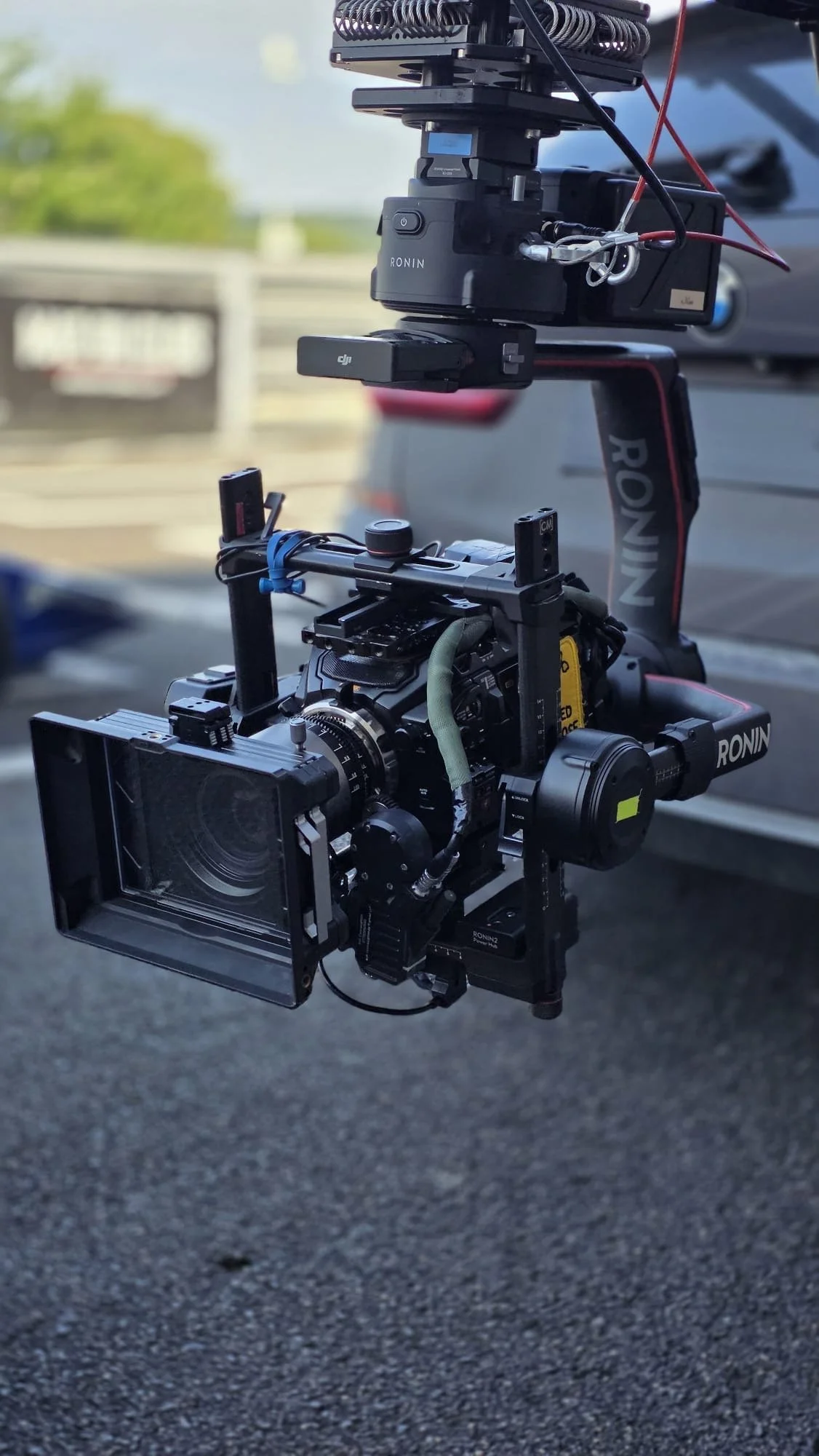A professional camera with a mounted stabilization gimbal rig, including an external monitor, is set up outdoors on a paved surface with a blurred background.