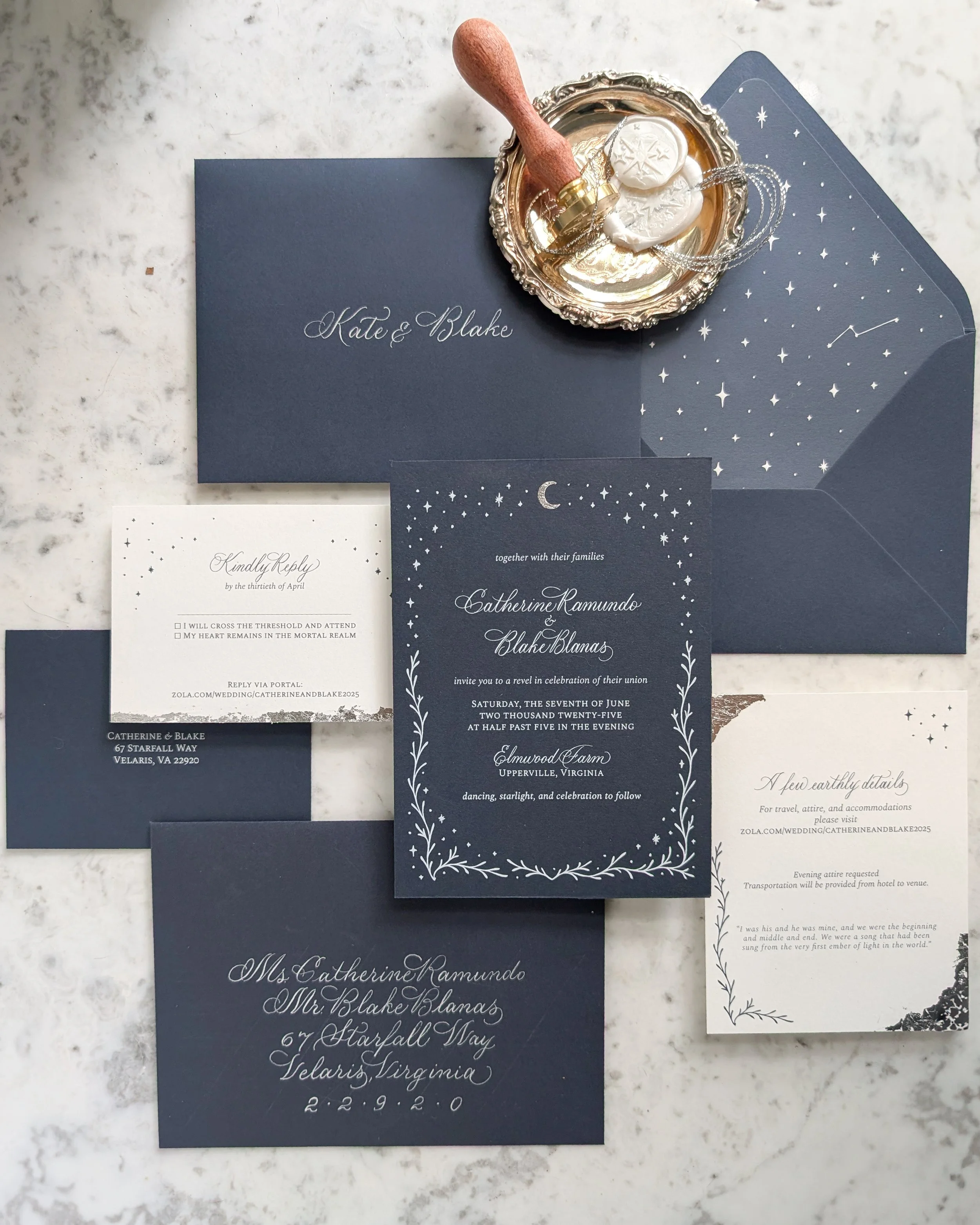 Flat lay of a custom wedding invitation suite with calligraphed envelope, silver thread wrap, and wax seal on blue paper with hand-applied silver leaf