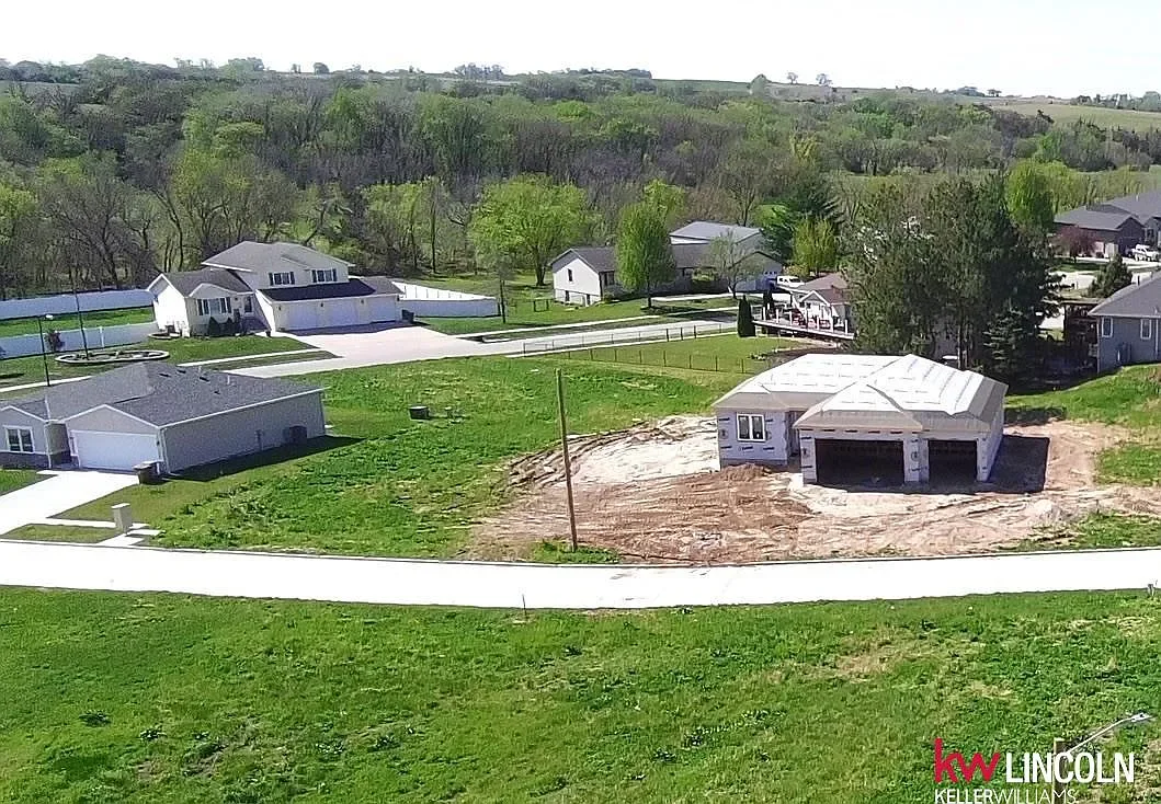 Residential neighborhood with houses, trees, and a house under construction with a white roof in a grassy yard.