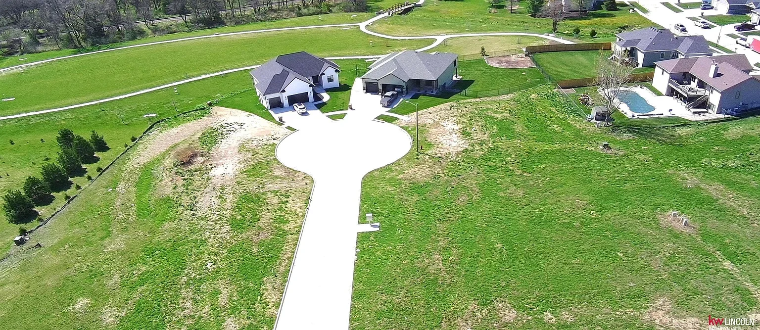 Aerial view of a suburban neighborhood with a large grassy hill, several houses with driveways, an in-ground pool, and some trees.