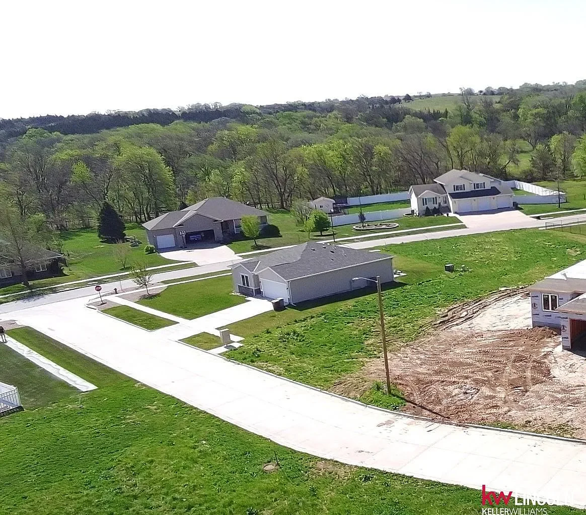 Aerial view of a suburban neighborhood with new construction houses, green lawns, trees, and a partly completed driveway and yard.