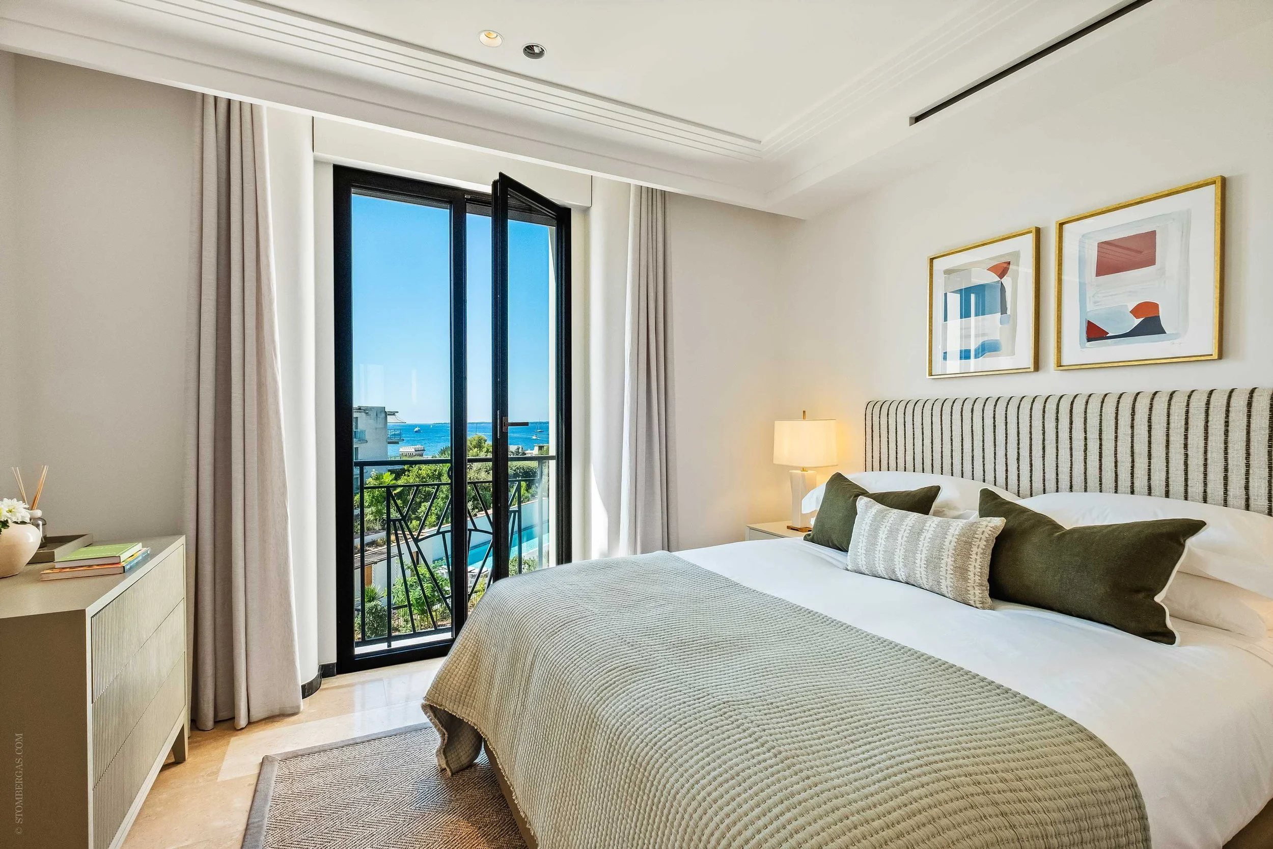 guest bedroom with stripey green headboard, abstract art on walls and green throw on bed, view out to the sea