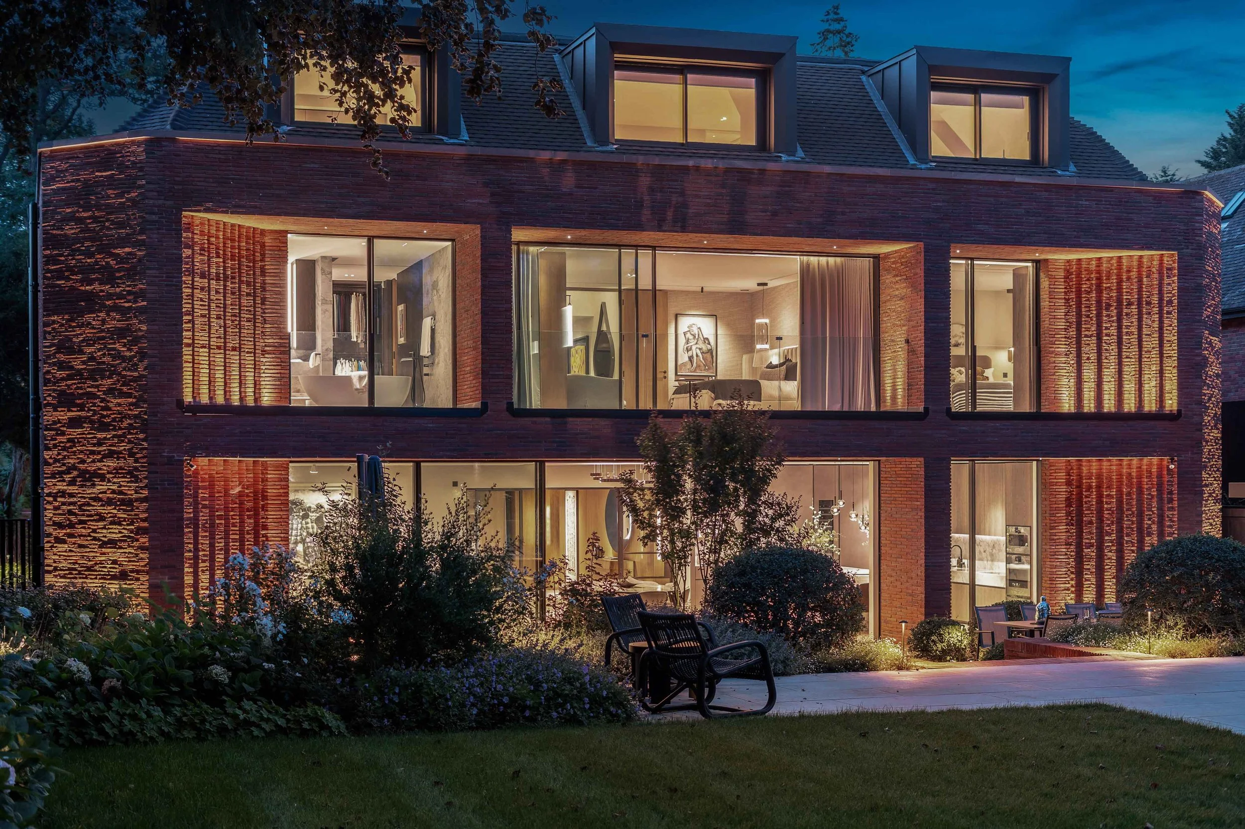Night time exterior photogarph of a large contemporary country house. each room is lit up so that you can see the interiors.