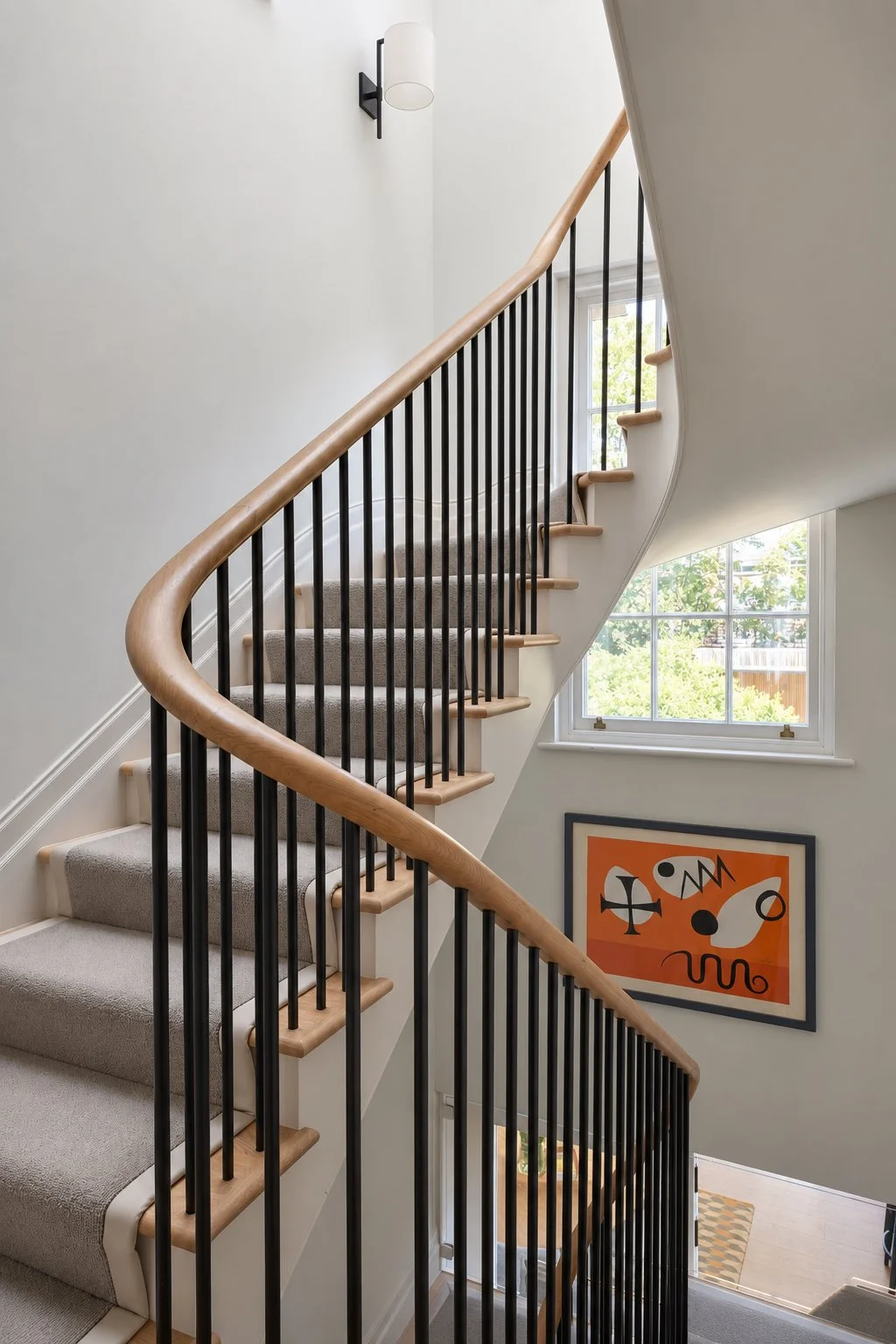 bold spiral staircase running through centre of townhouse with soft grey runner and orange artwork on the walls