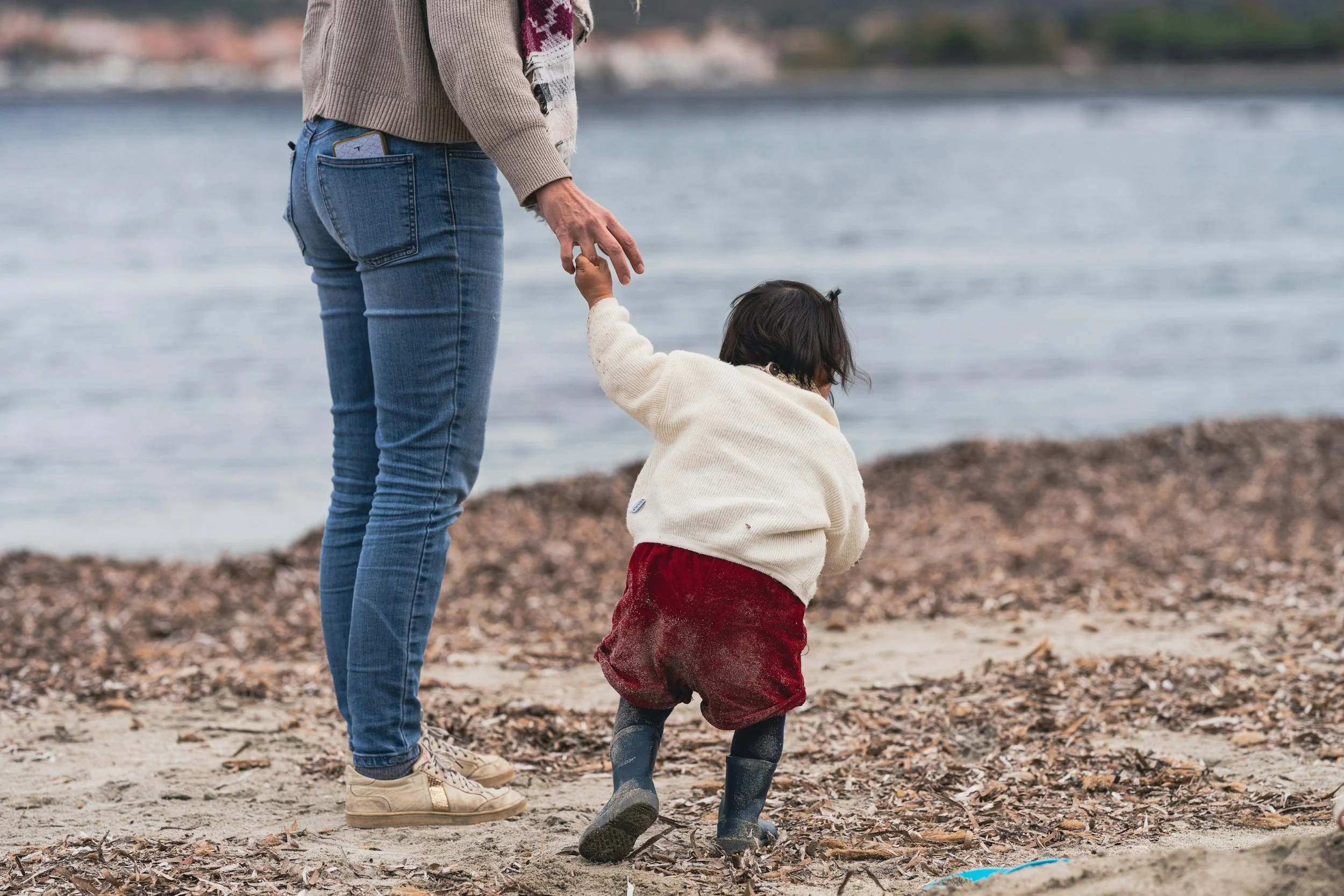 Parent holding a young child's hand while walking along a beach, representing family transitions, parenthood, and relationship changes after welcoming a child.