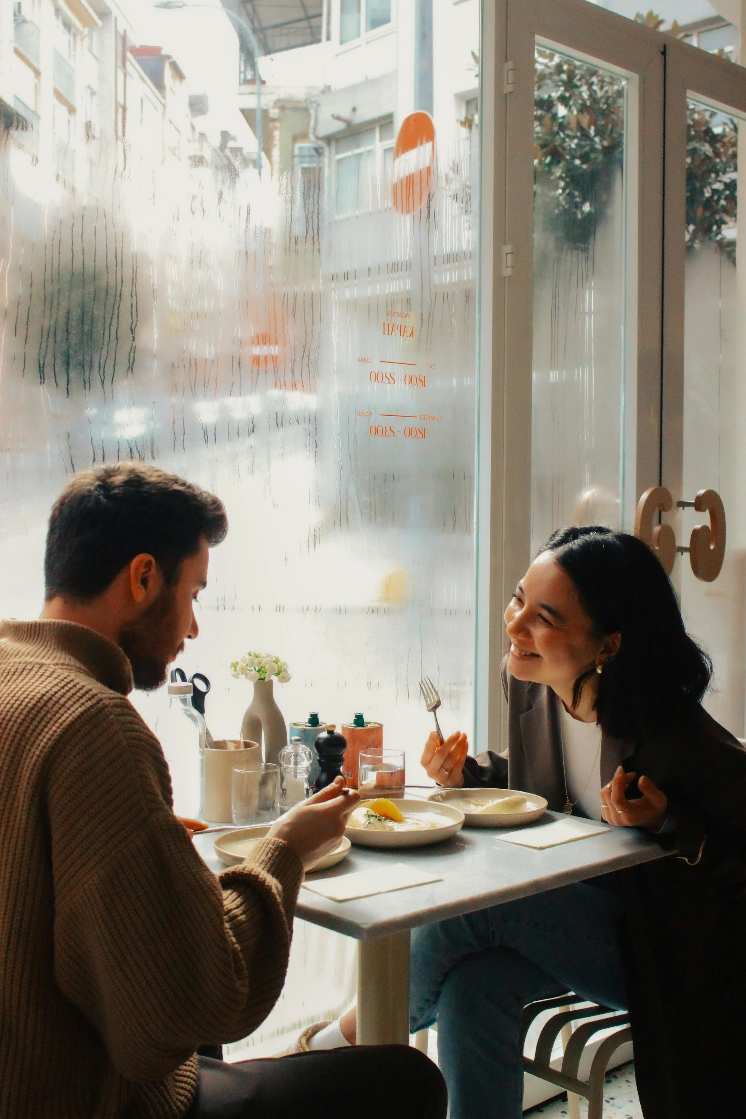 Two people sitting at a table having coffee together, smiling and engaging in a warm, meaningful conversation, illustrating connection and relational support.