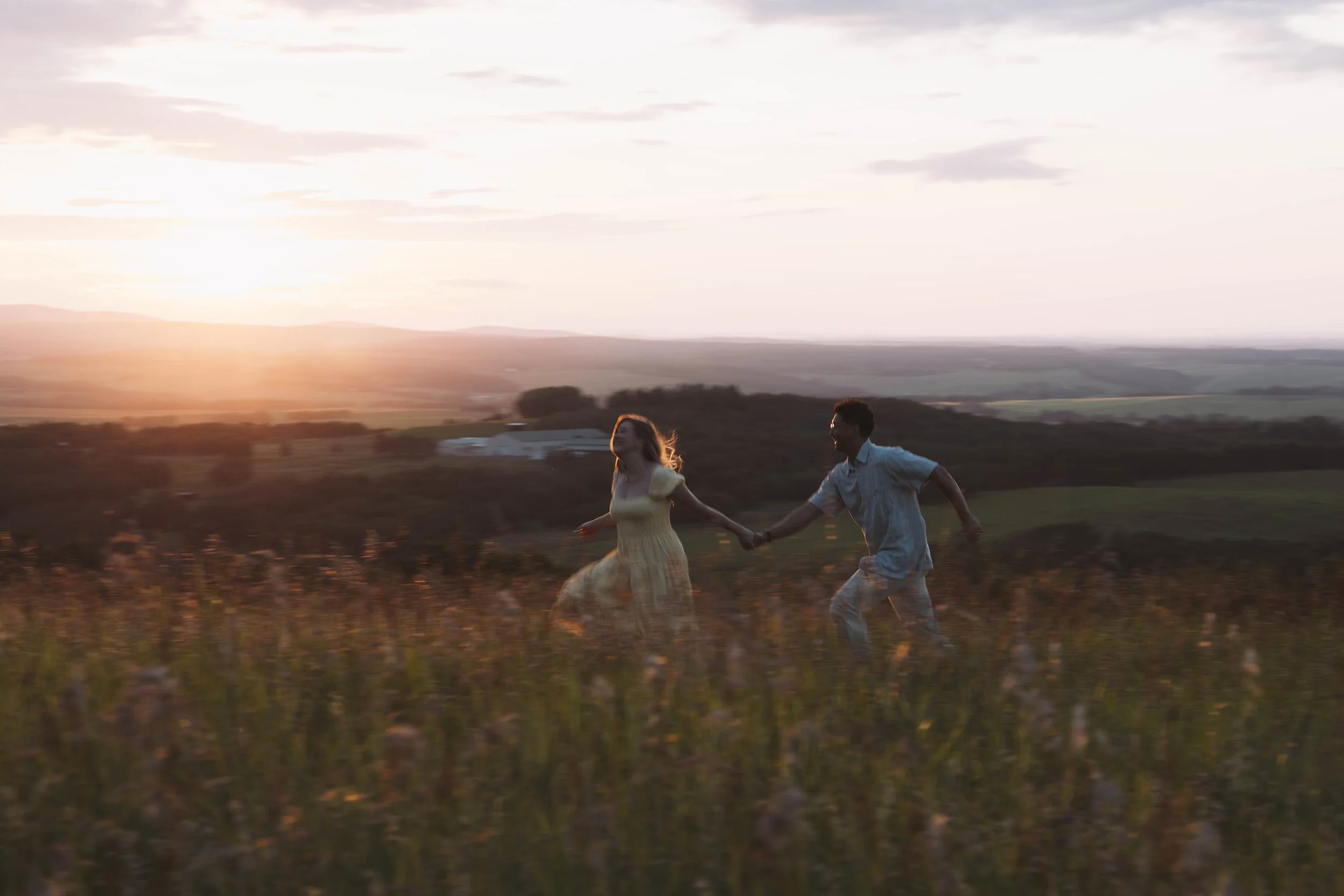 A couple running hand in hand through a field during sunset.