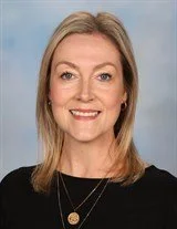A woman with shoulder-length blonde hair wearing a white top and green cardigan, smiling for the photo.