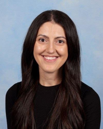 Portrait of a woman with shoulder-length blonde hair, wearing a white top with blue floral patterns, smiling, against a plain background.