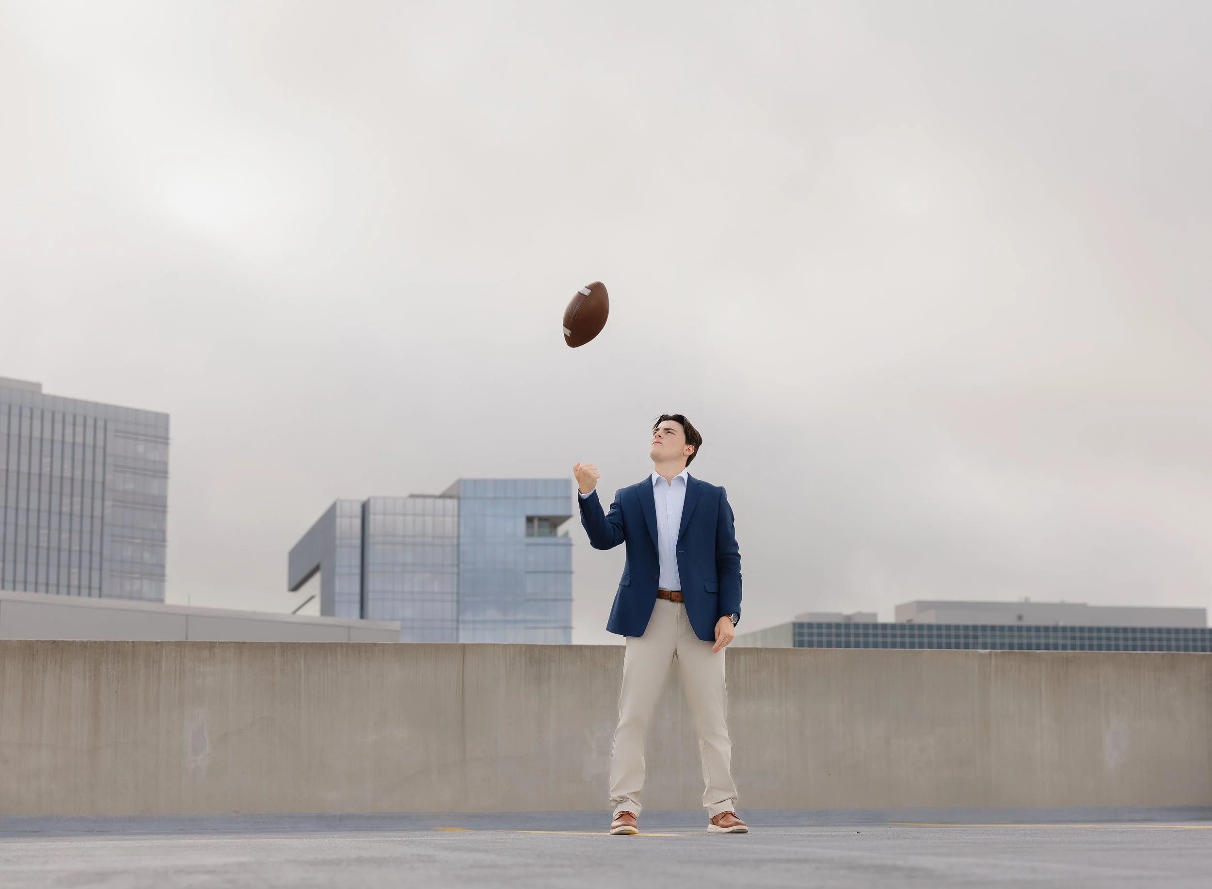 Senior in high school tossing a football on the roof of a parking garage in a suit
