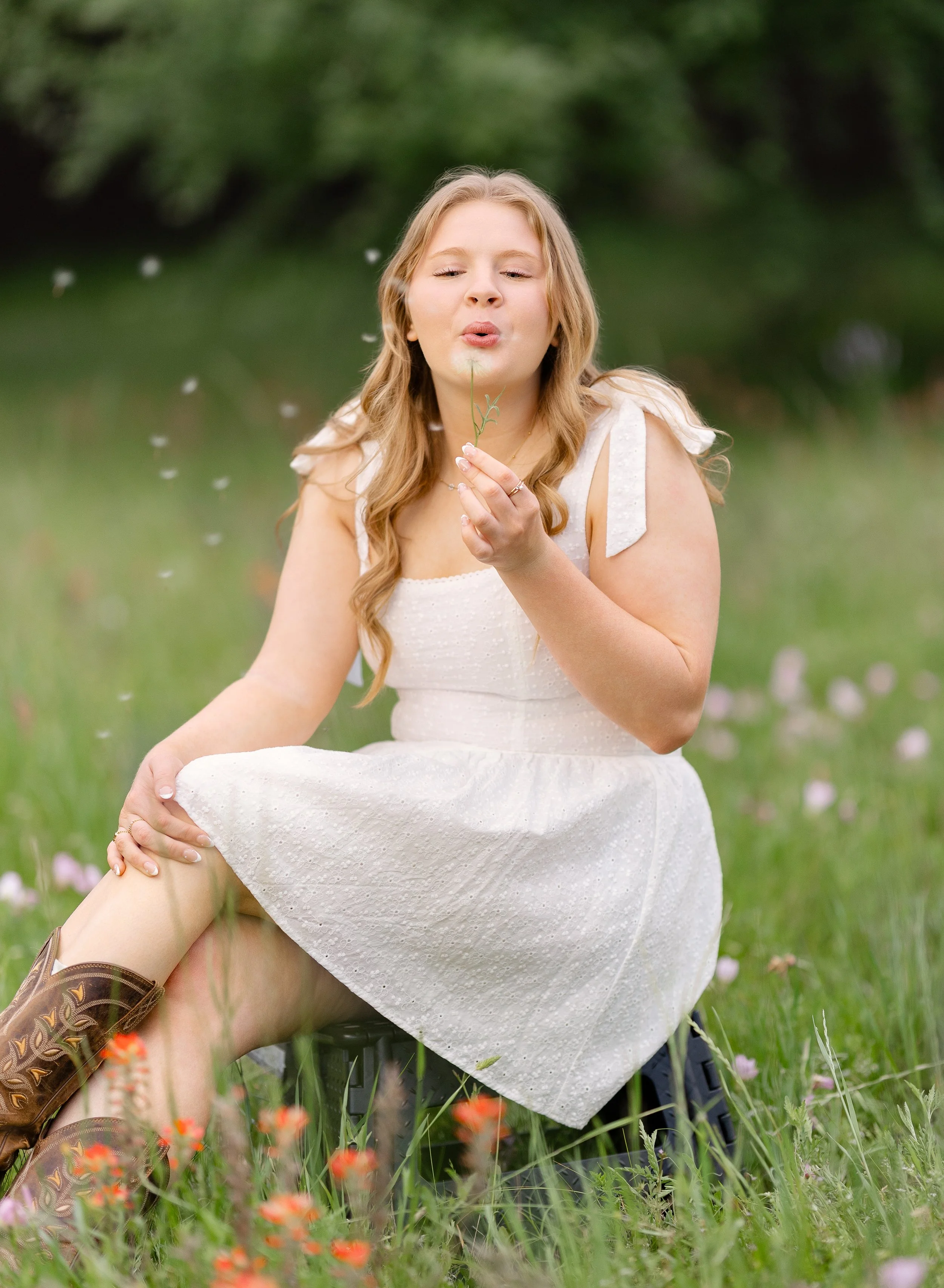 High School Senior blowing a dandelion in a white dress