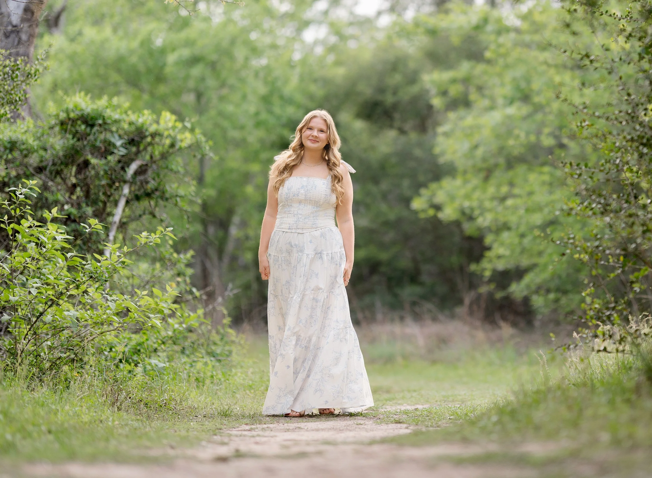 High school girl with blond hair walking in the woods in a blue and white floral dress