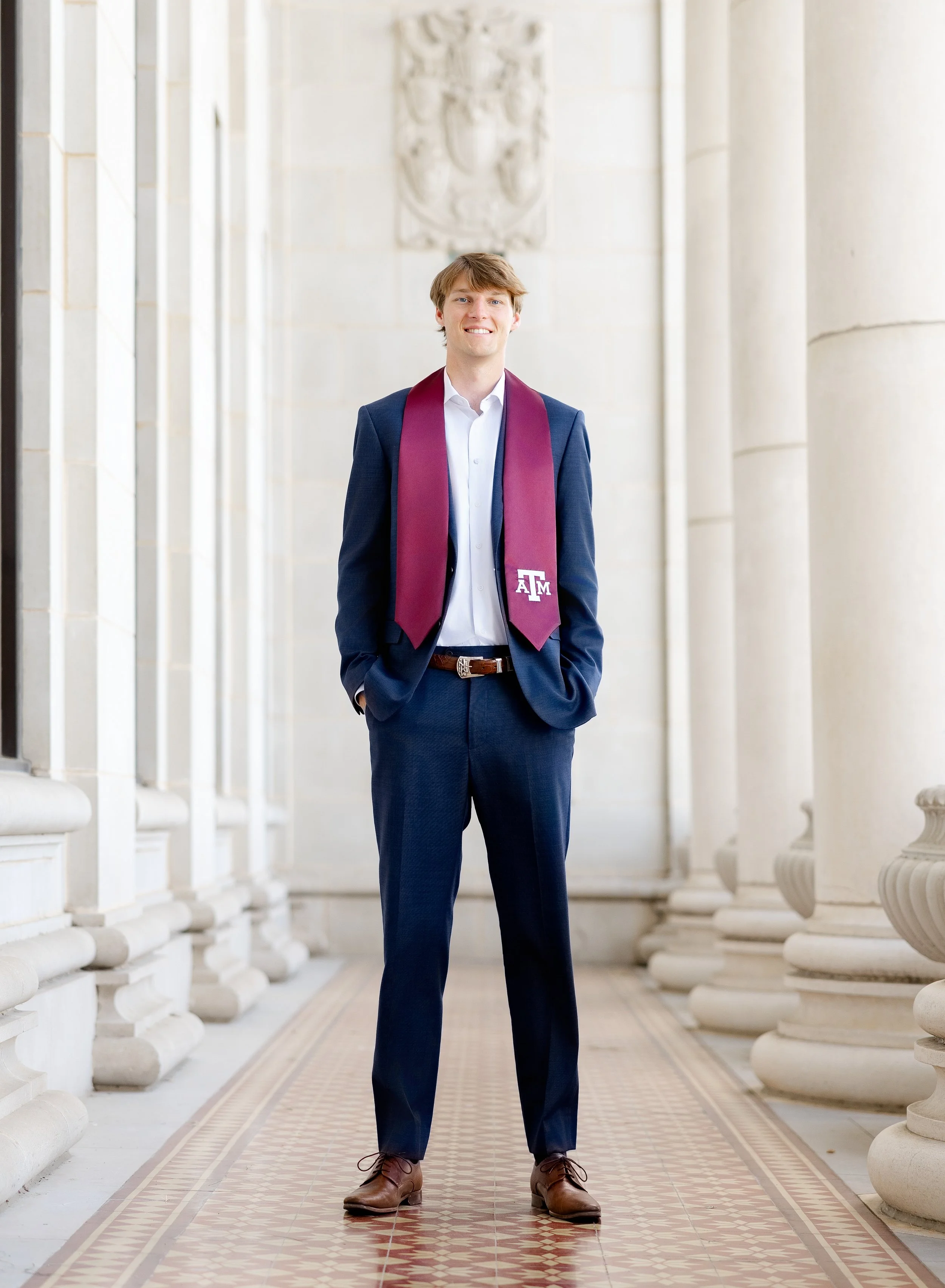 Yong man in a suit with a maroon Aggie stole posing at the Administration building