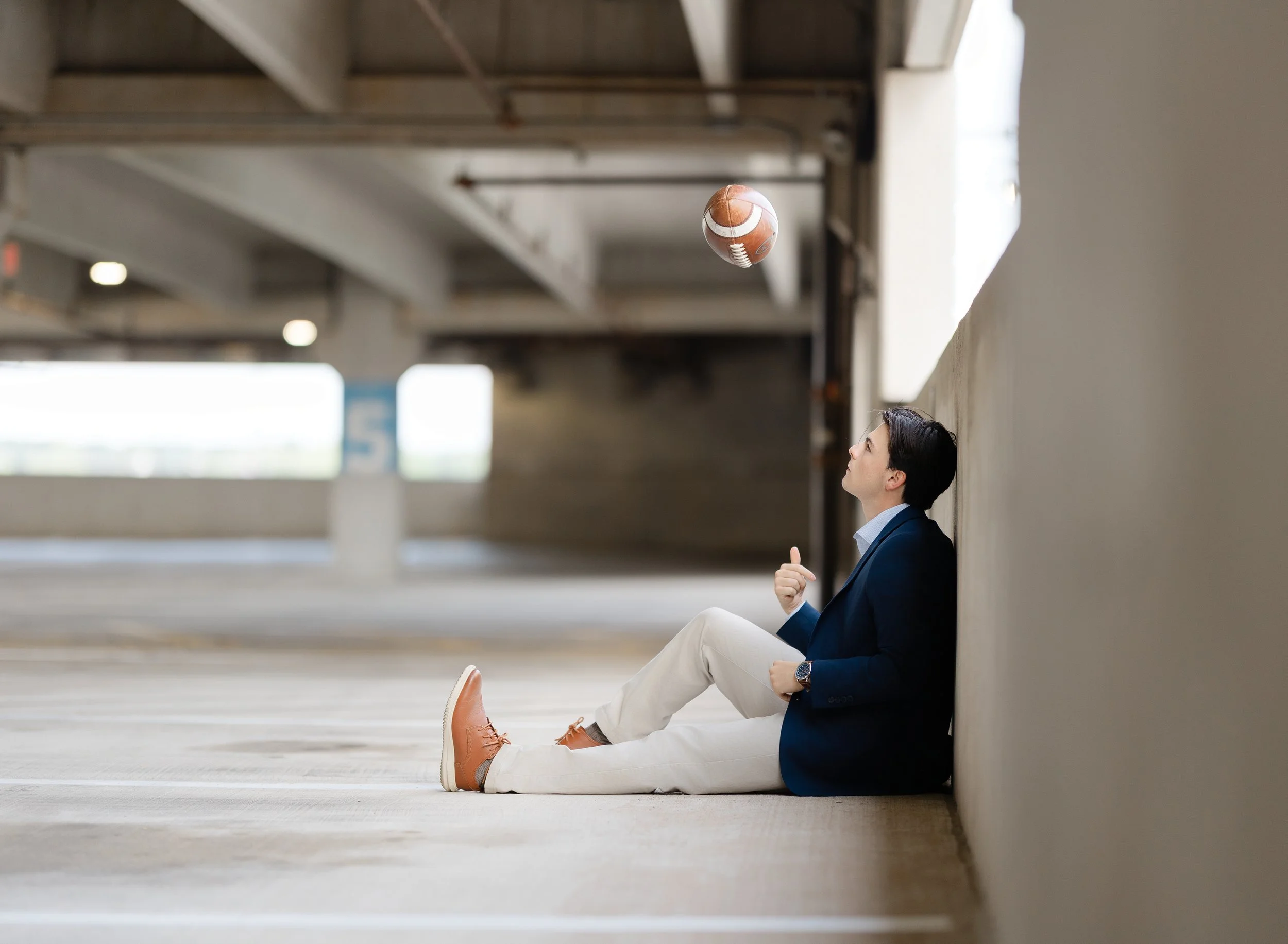 Senior in High school in a parking garage in a suit tossing a football