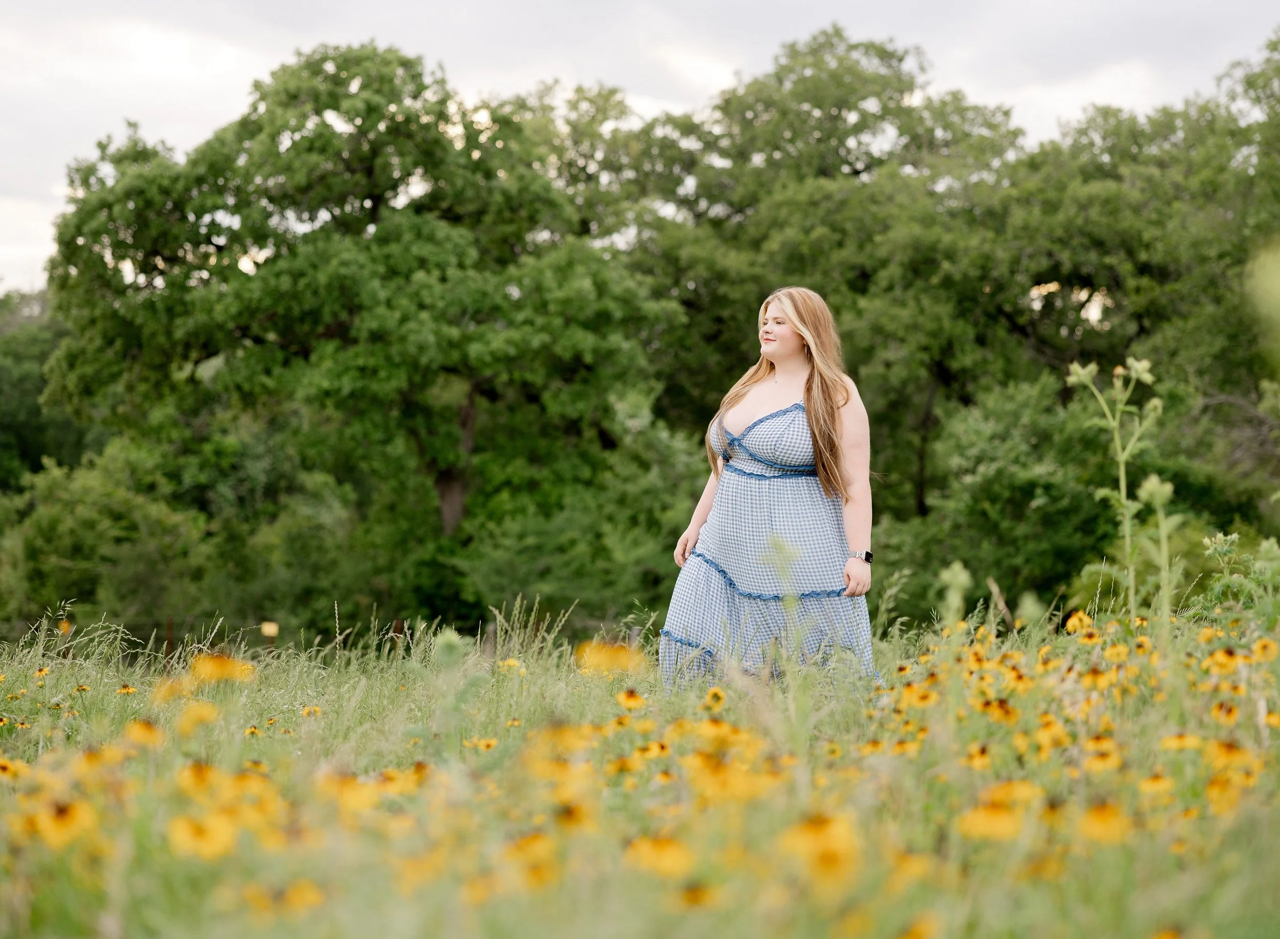 Girl with blond hair in a gingham dress walking through a field of black eyed susans