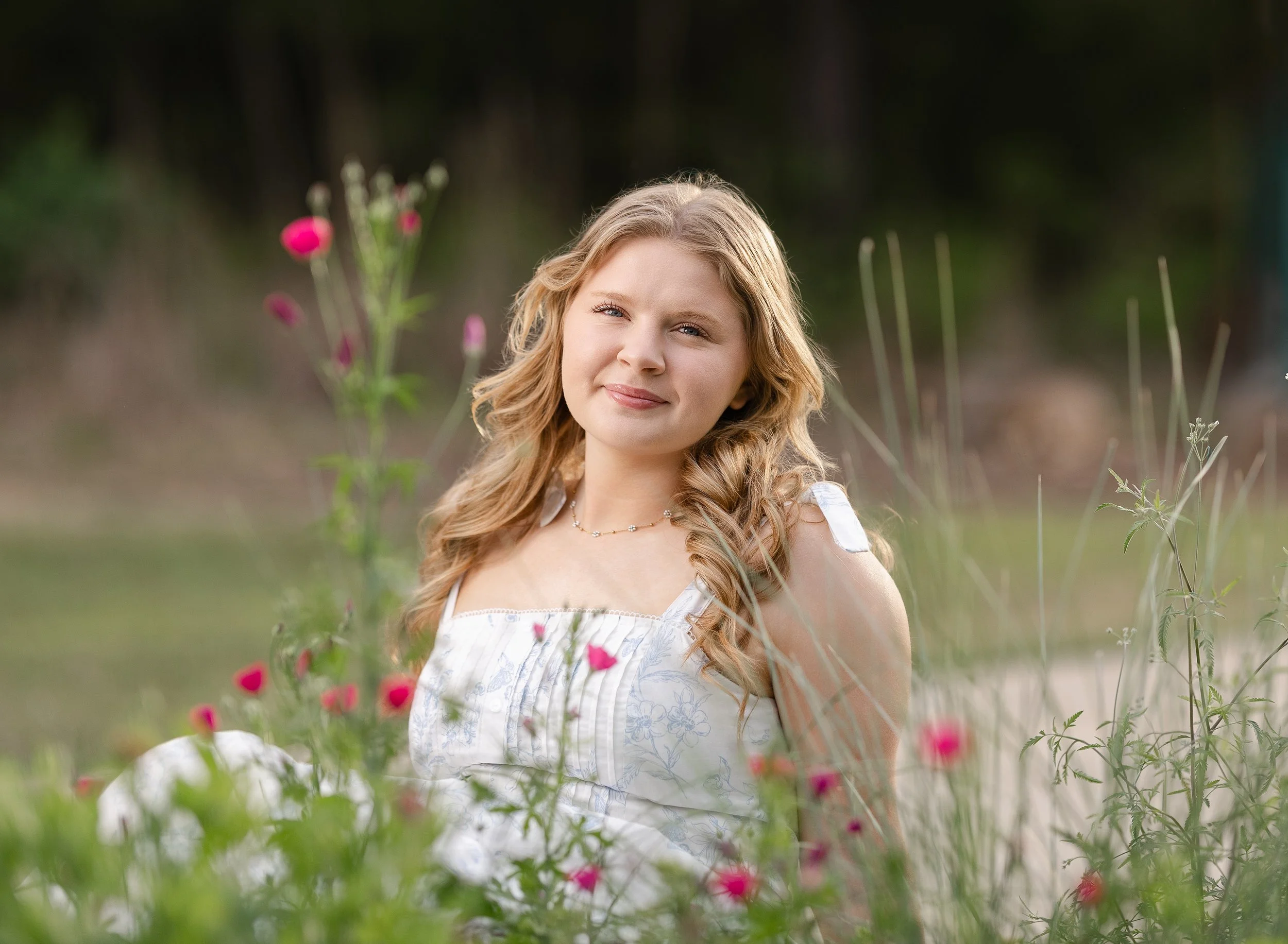 High School Senior wearing a white and blue dress sitting in the flowers