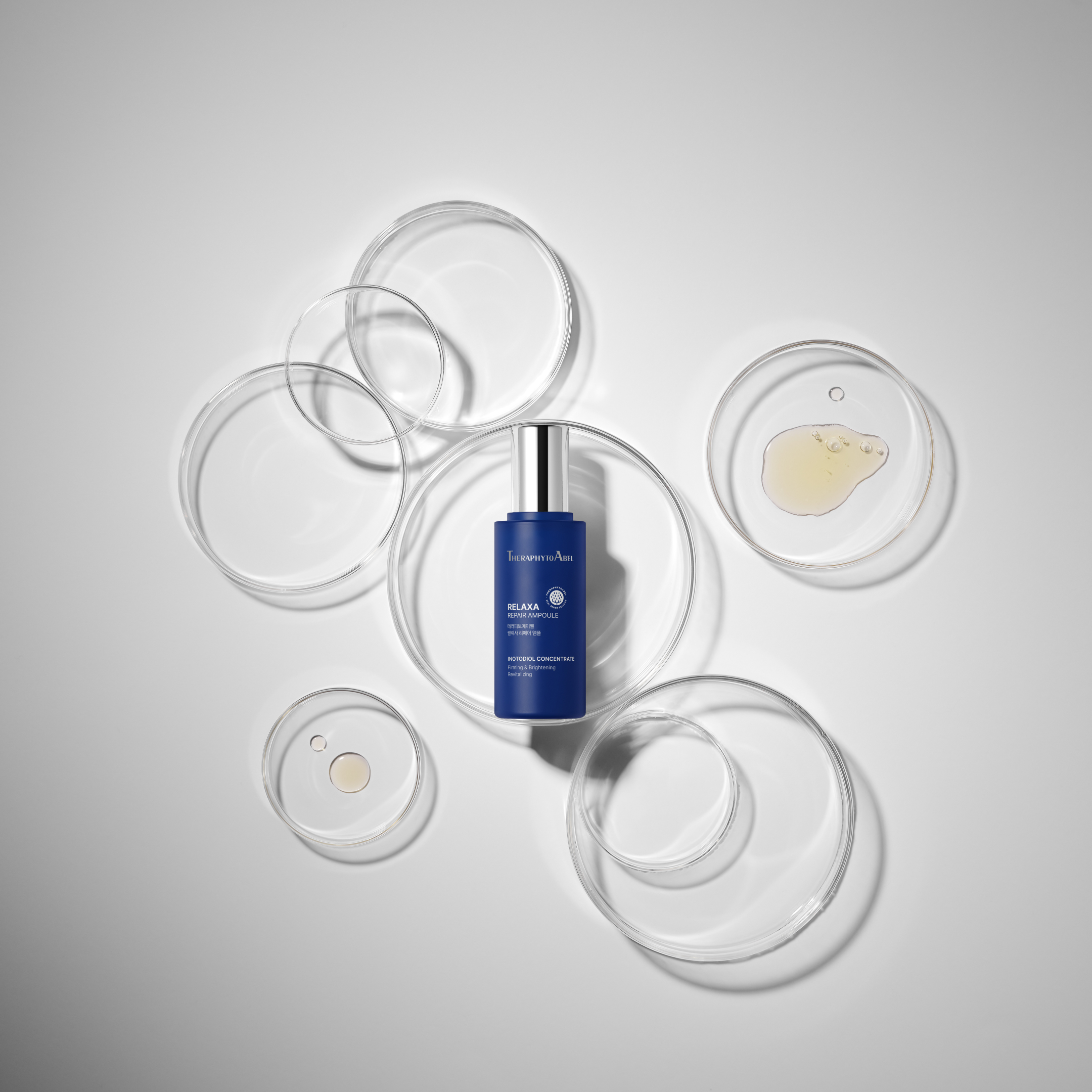 A blue bottle of TheraphytoAbel Relaxa Repair Ampoule surrounded by several empty and partially filled glass petri dishes on a white background.