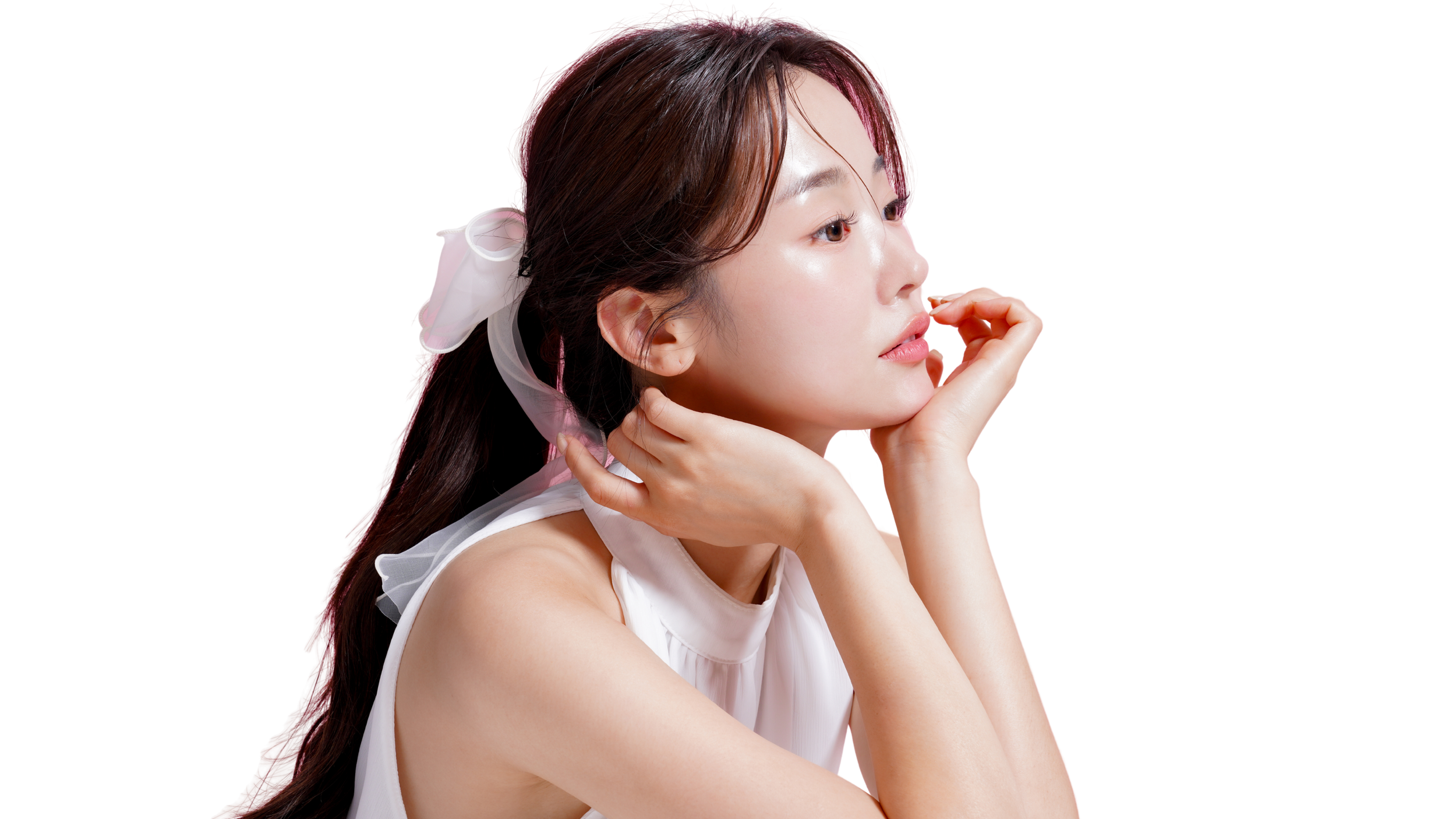 A young woman with long brown hair, styled with a white bow, rests her chin on her hand with a thoughtful expression, wearing a sleeveless white top.