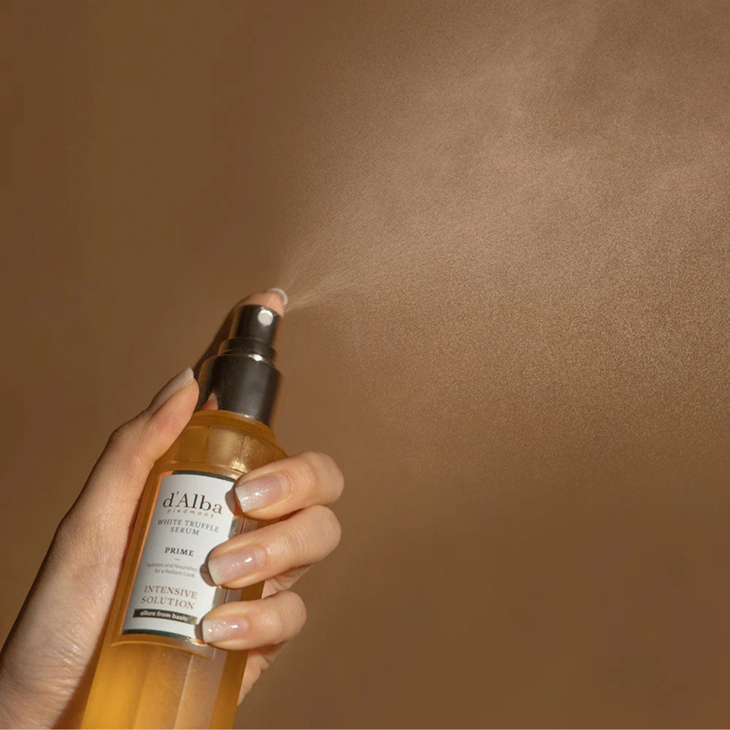 A hand holding a spray bottle labeled 'd'Alba White Truffle Serum,' spraying a fine mist against a light brown background.