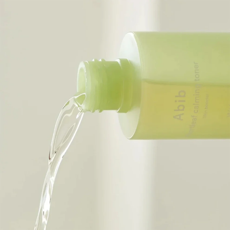 A close-up of a light green bottle with clear liquid being poured out of it.