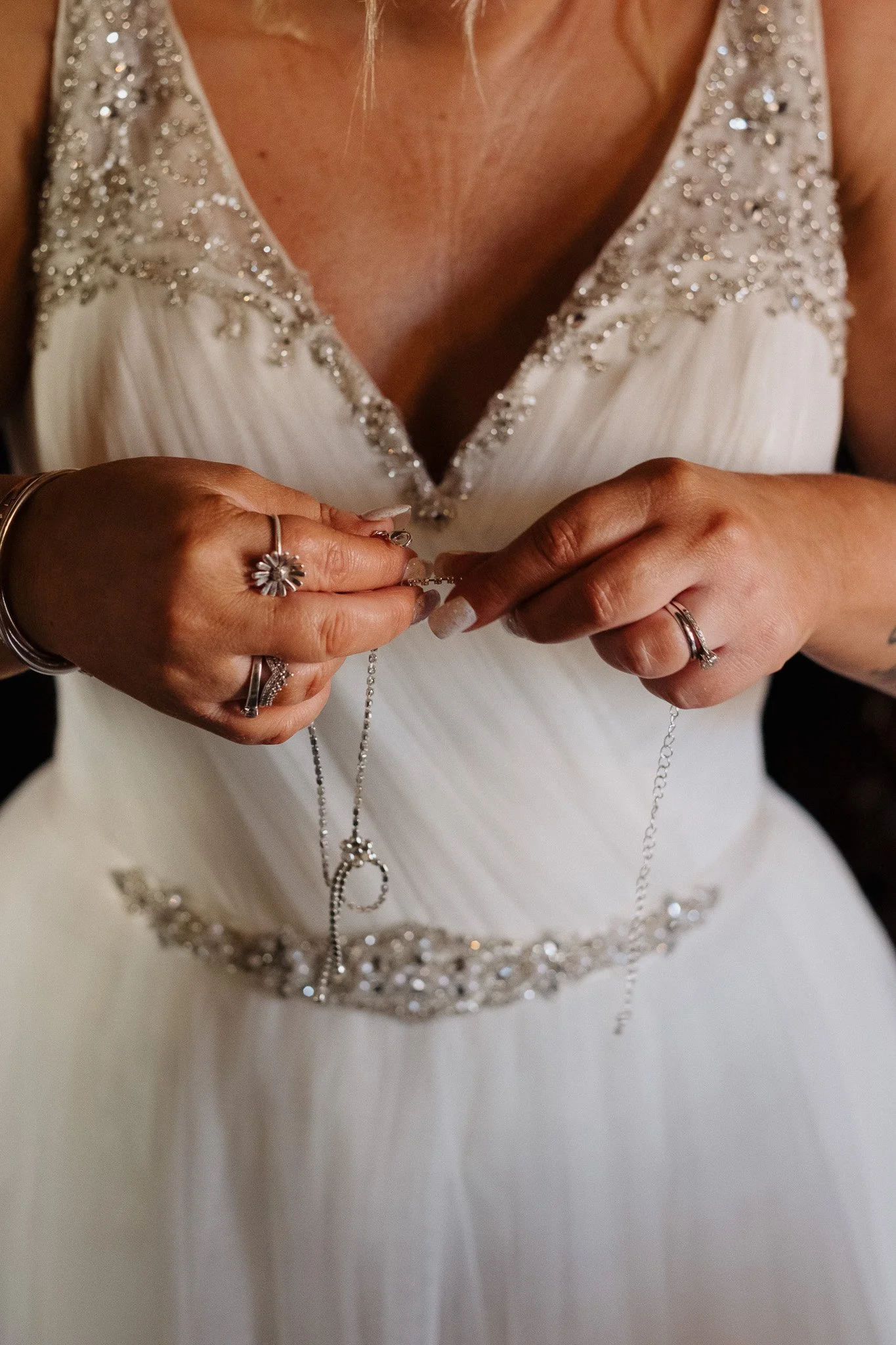 Bride holding a necklace while wearing a white wedding dress with beaded embellishments.