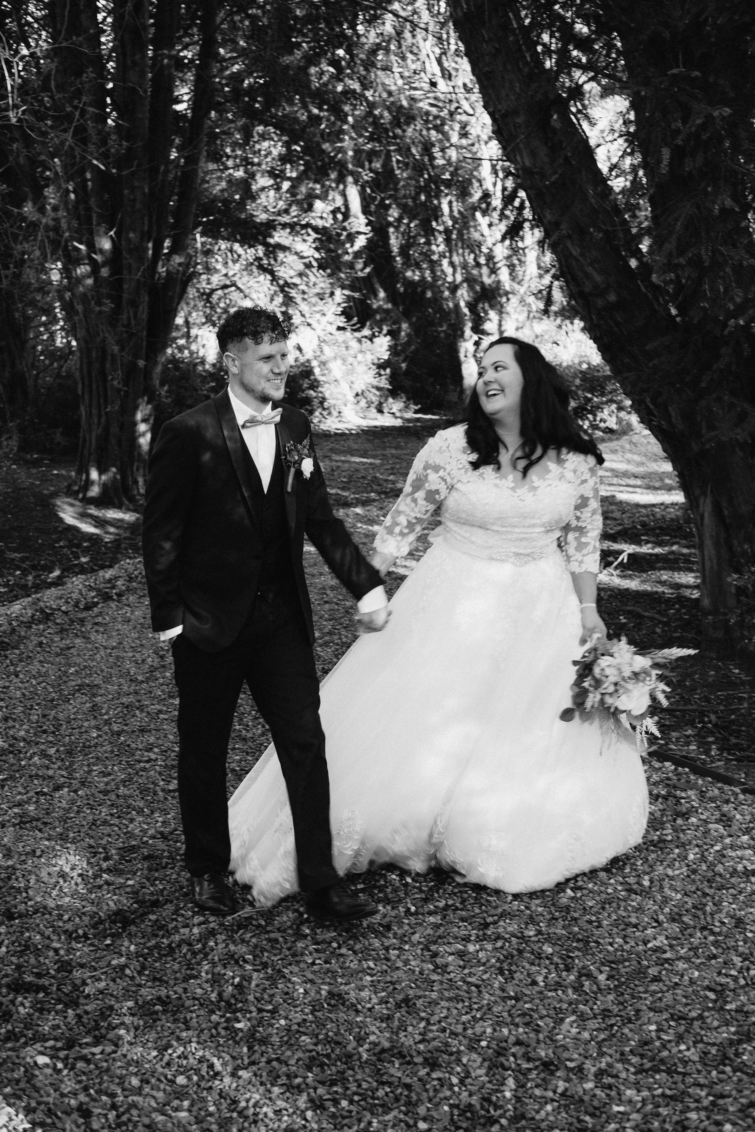 Bride and groom walking outdoors, holding hands, black and white photo