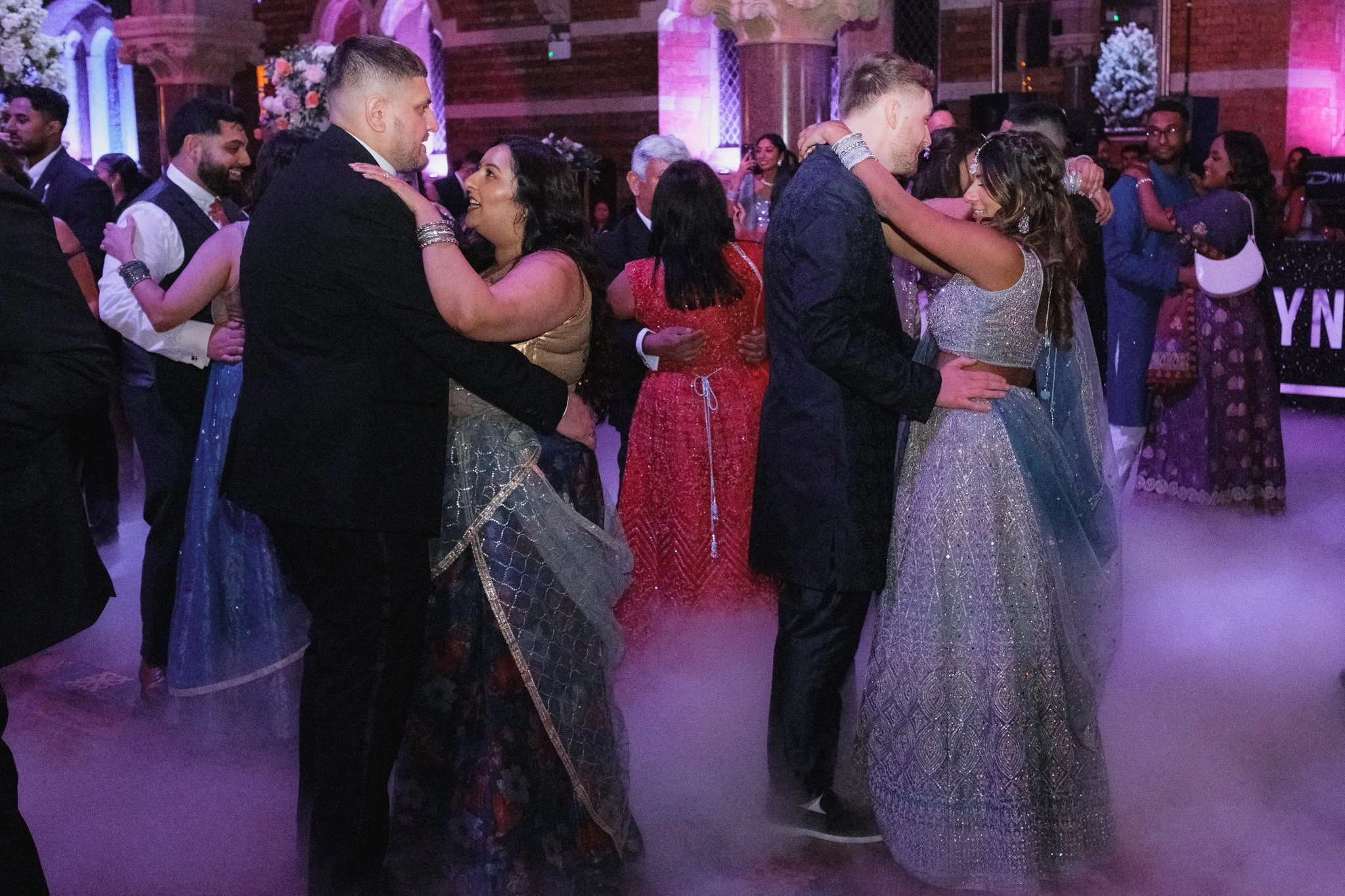 Couples dancing at a formal event with atmospheric lighting and fog.