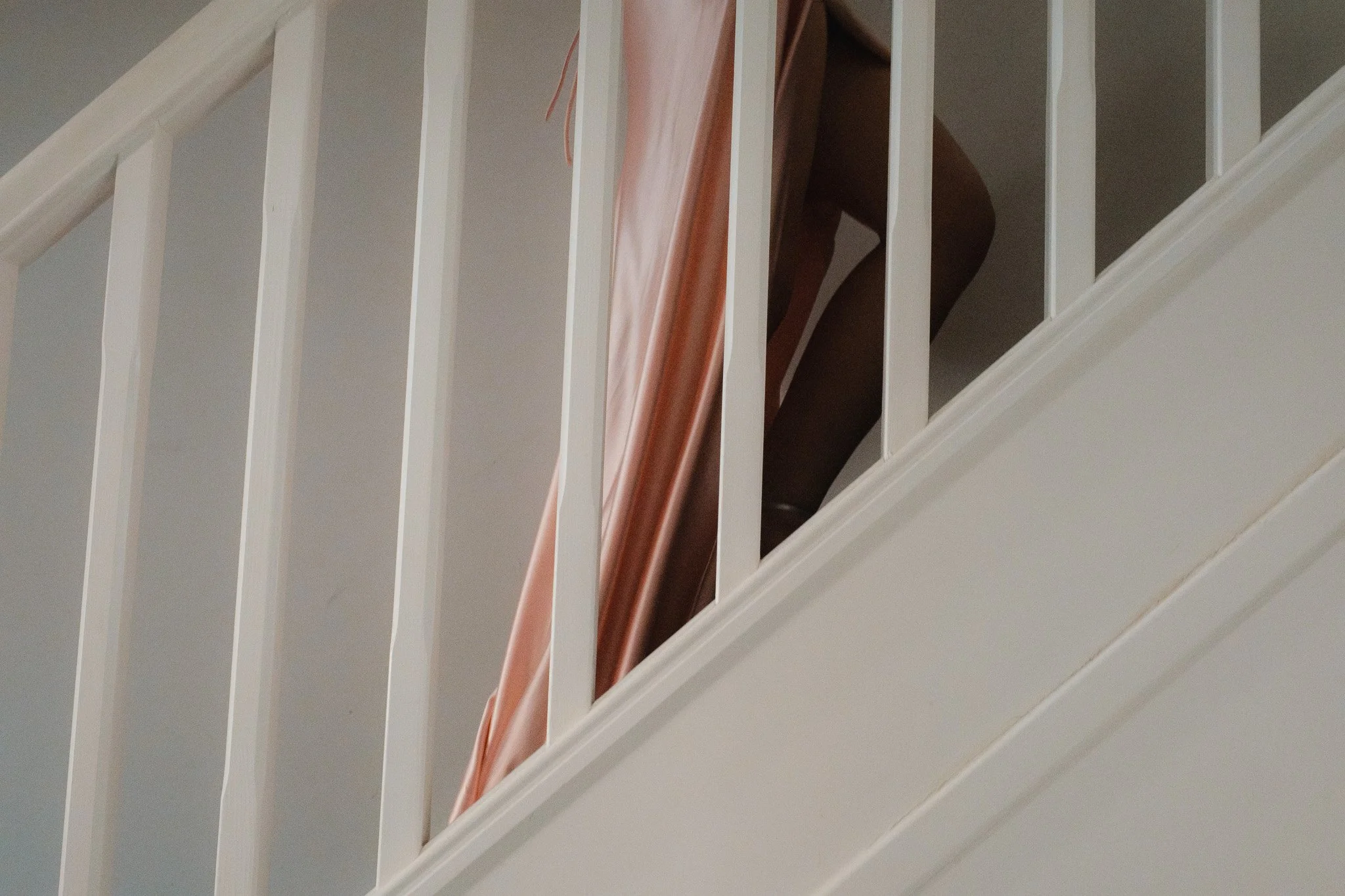 Person in a flowing peach robe ascending a staircase with white railings.