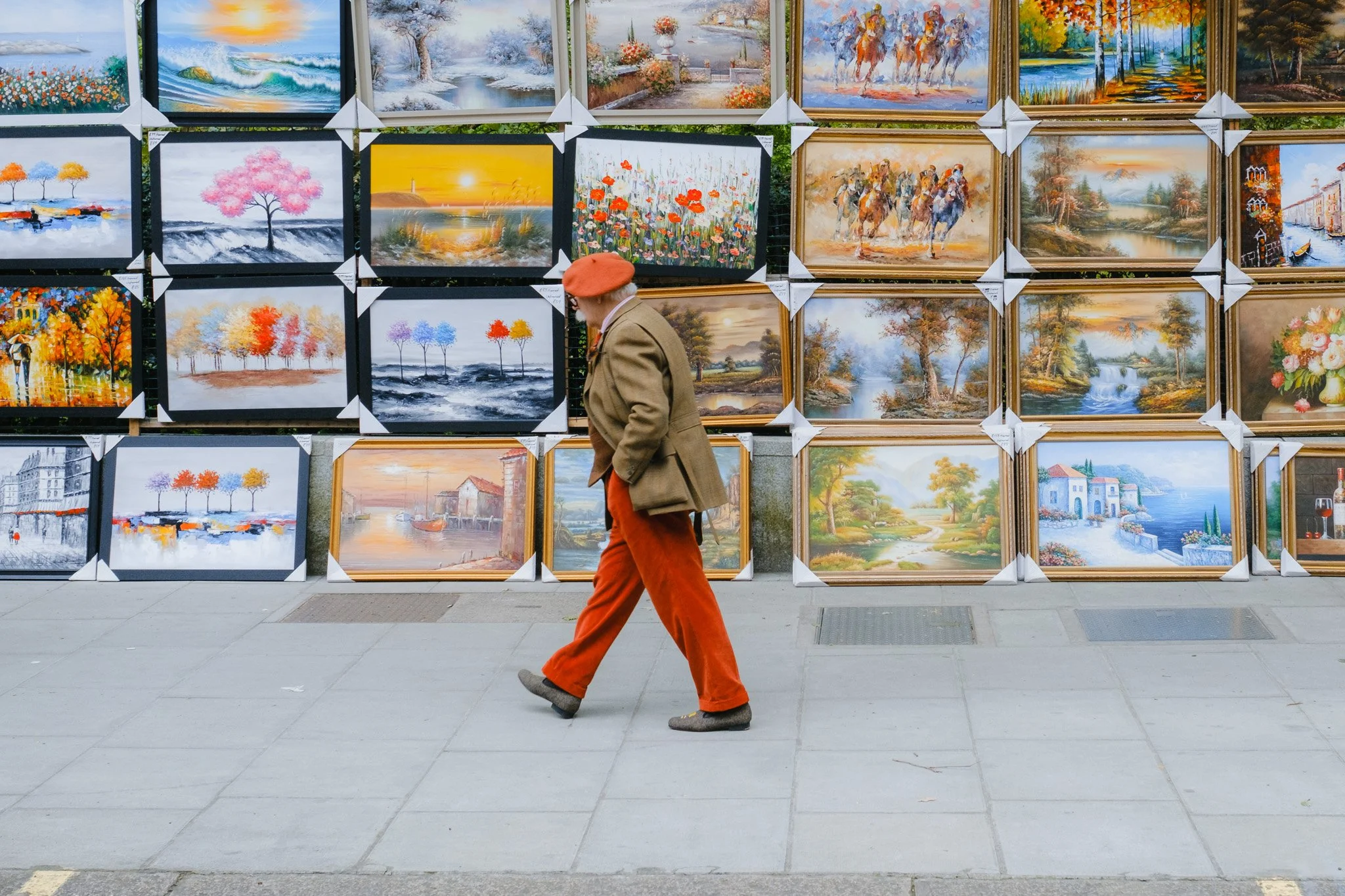 Man walking in front of a display of colorful paintings on a sidewalk.