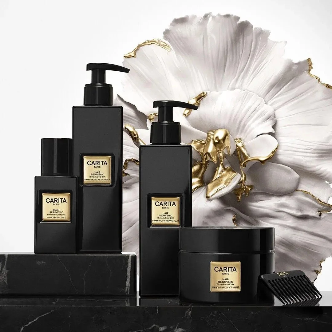 Carita Hair Rejuvenic shampoos, restructuring mask and protective oil in black and gold packaging, displayed with a white and gold sculptural flower.