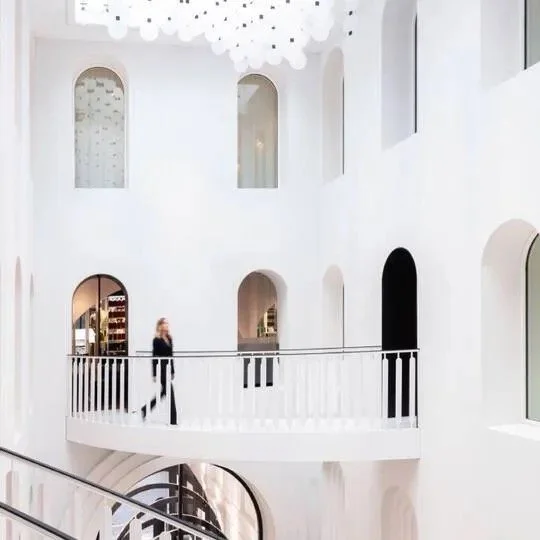 White atrium and upper galleries at Maison de Beauté Carita, with arched openings, a curved staircase and hanging lights.